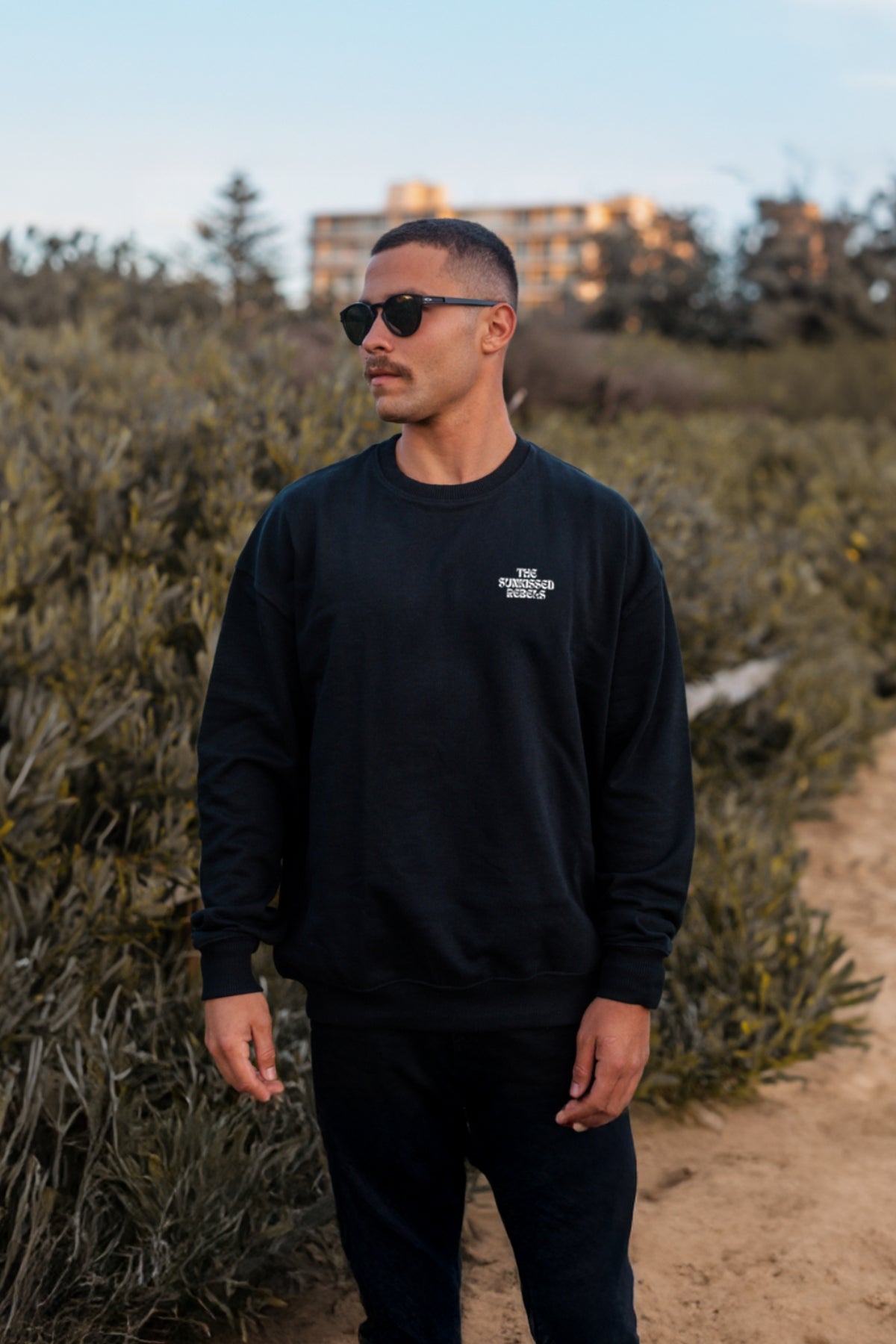 Man trägt schwarzen oversized Sweater von The Sunkissed Rebels am Strand. 