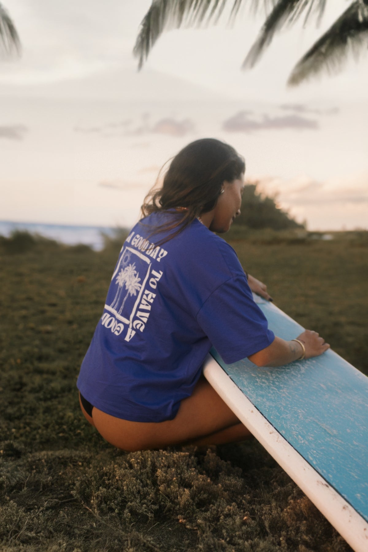 Surferin wachst Surfbrett und trägt lila T-Shirt 