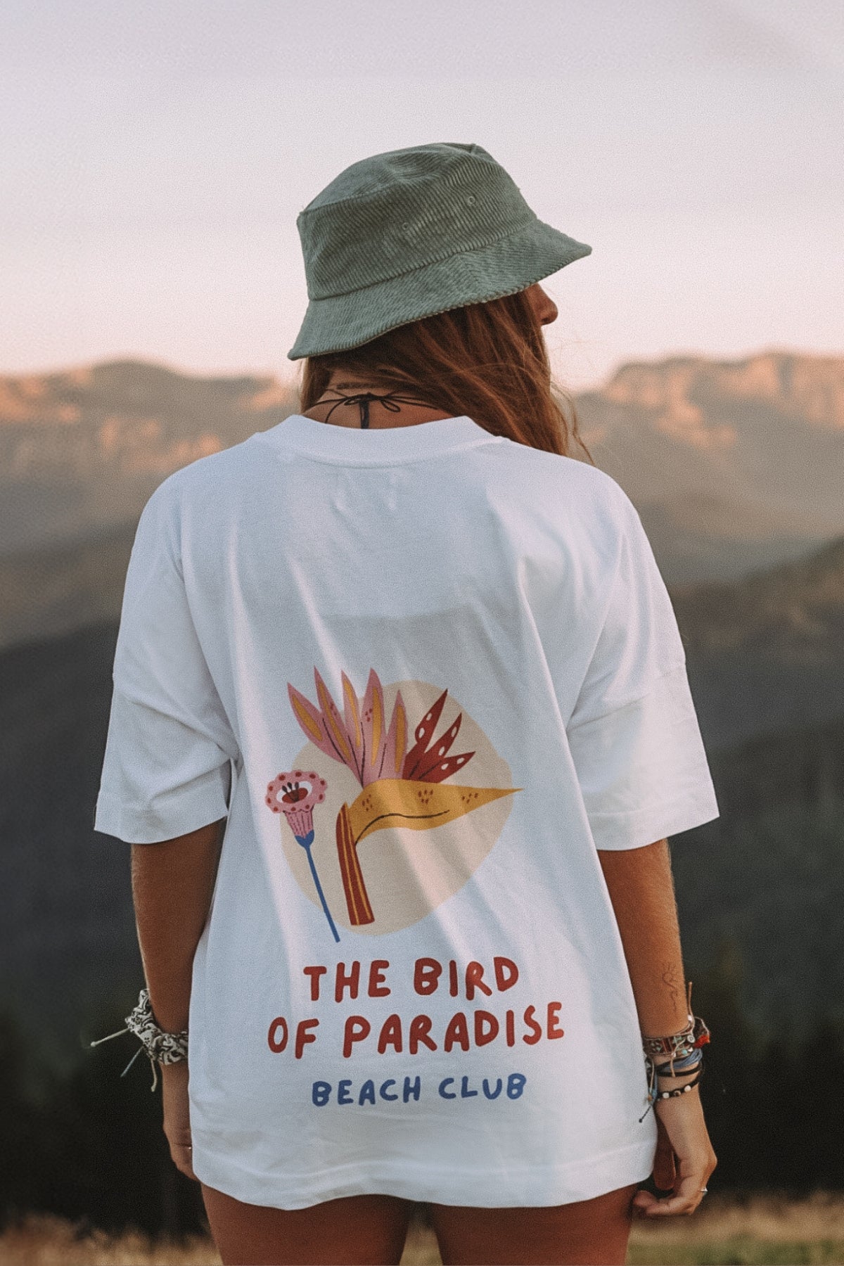 Frau schaut auf die Berge und trägt das Bird of Paradise T-Shirt von The Sunkissed Rebels
