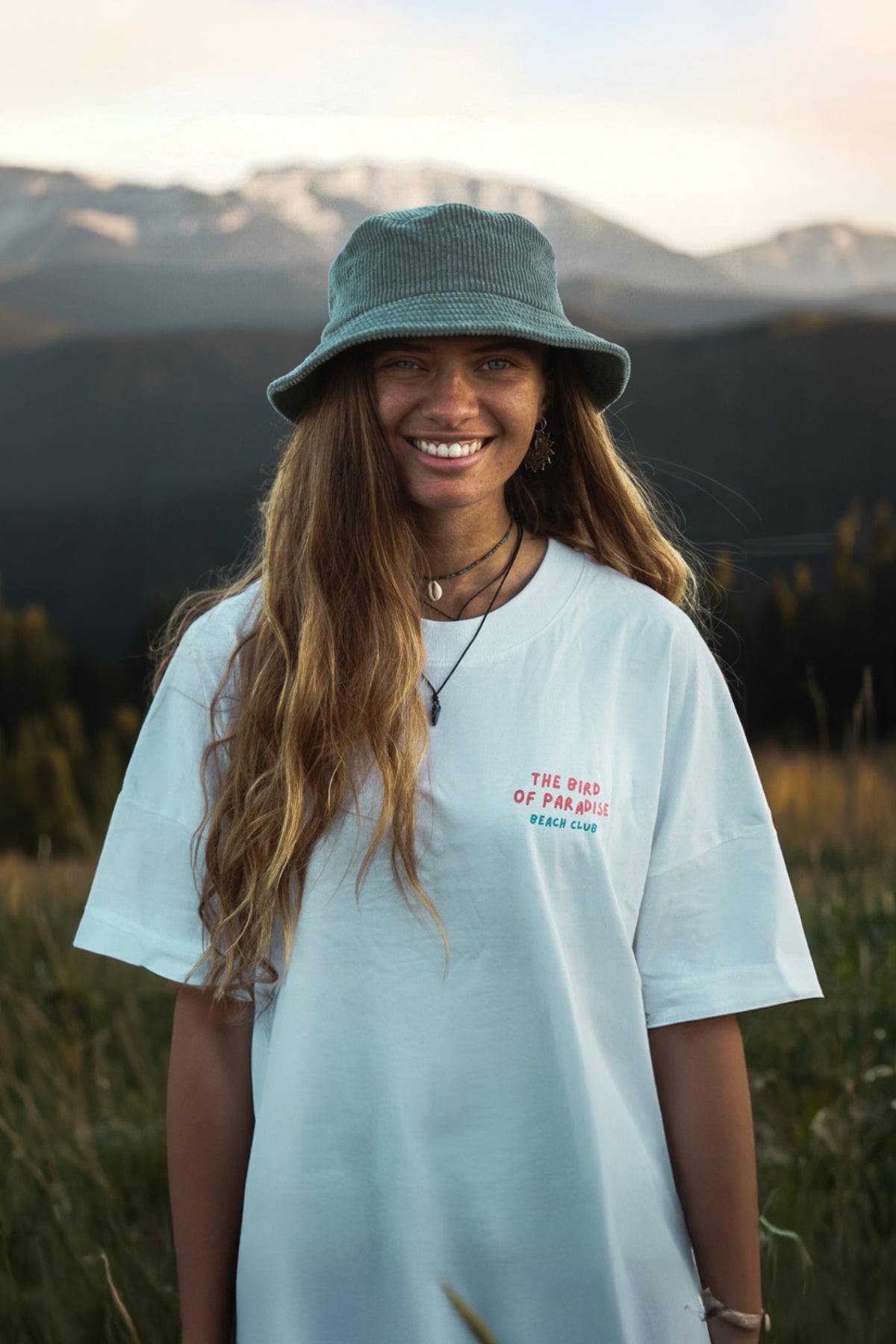 Frau steht in den Bergen und trägt dabei das Bird of Paradise T-Shirt von The Sunkissed Rebels. 