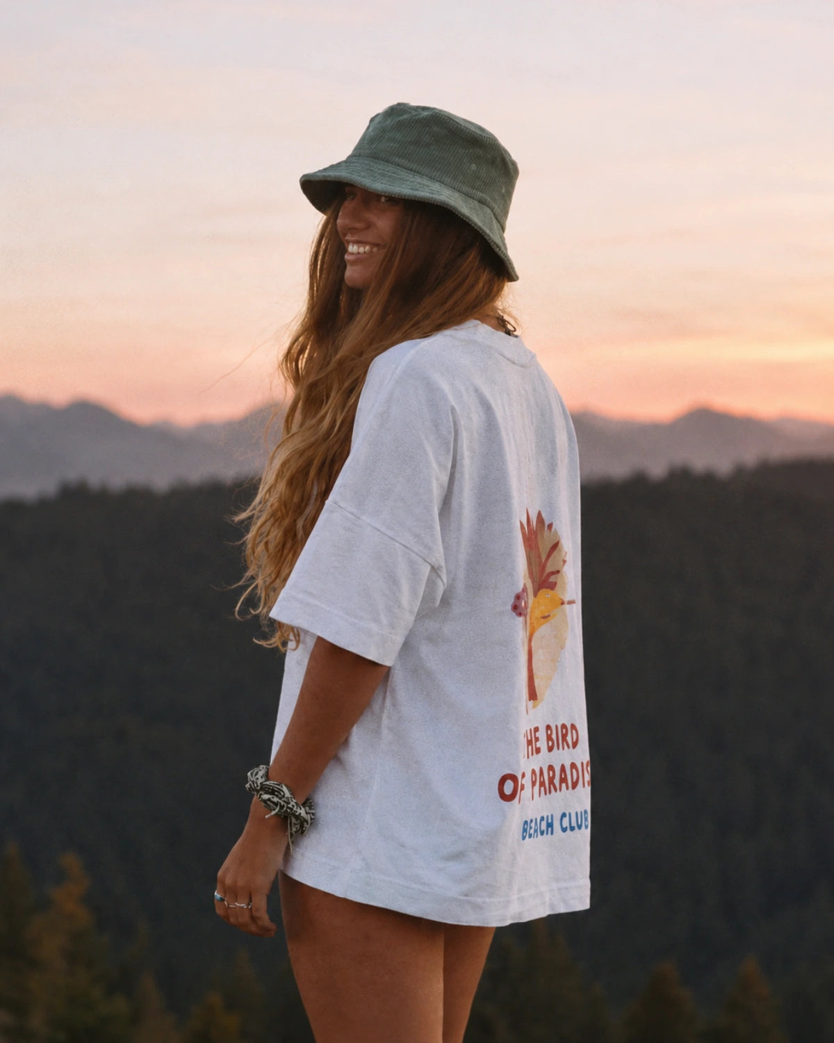 Frau trägt das Bird of Paradise Oversized T-Shirt in White mit großem Bird of Paradise Rückenprint in den Bergen