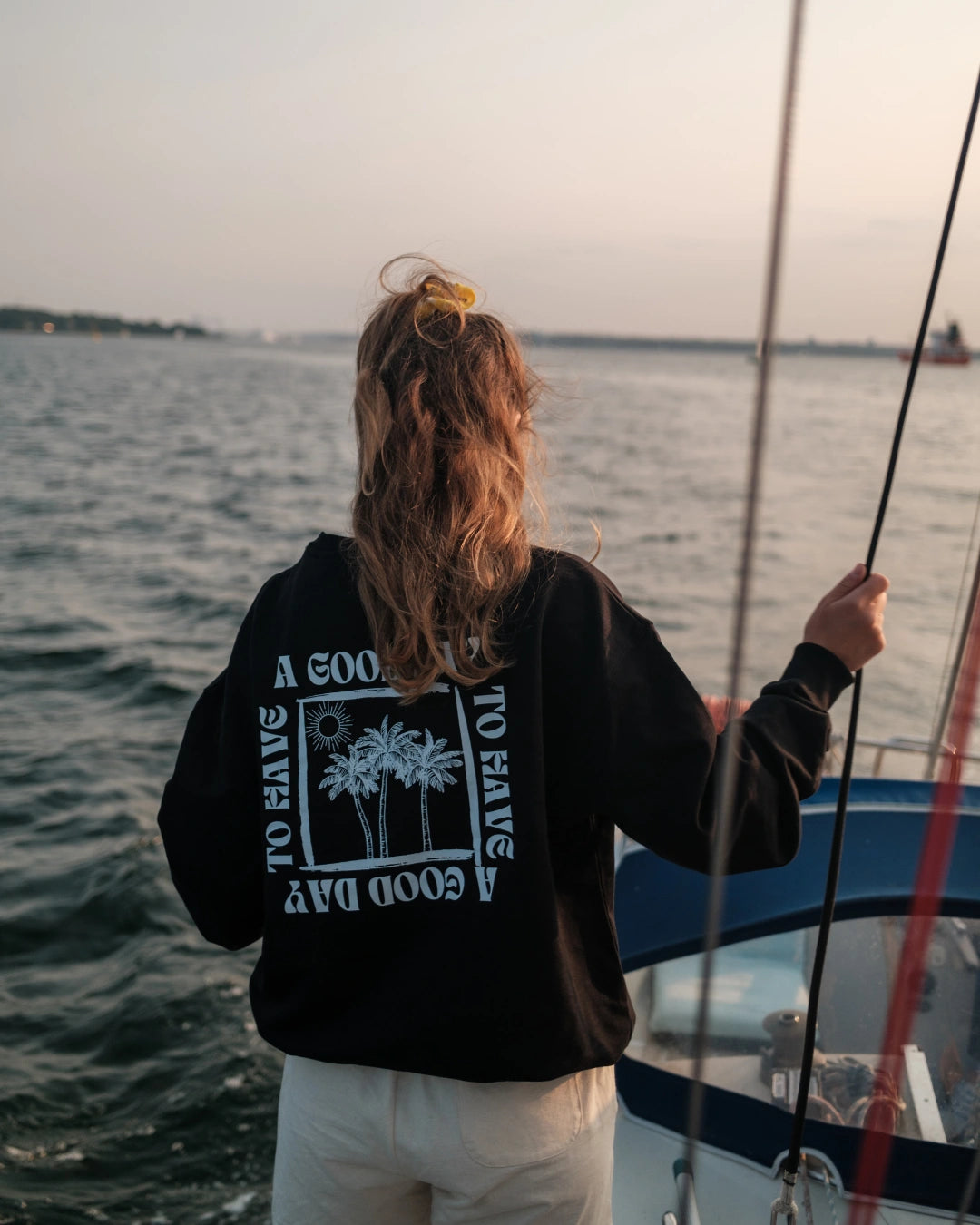 Frau auf Segelboot trägt schwarzen A Good Day Sweater Rückansicht 