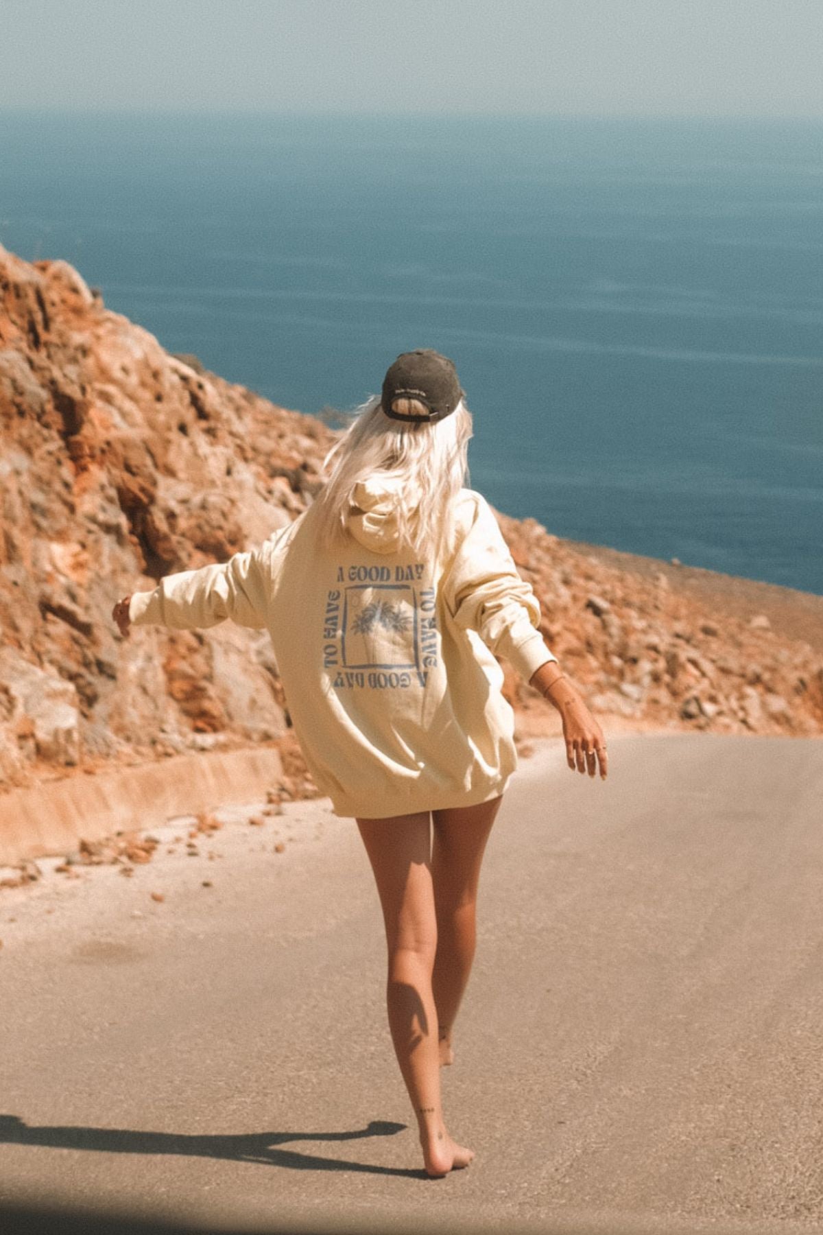 Frau läuft auf langer Straße Richtung Meer und trägt dabei einen Oversized Hoodie von The Sunkissed Rebels. 