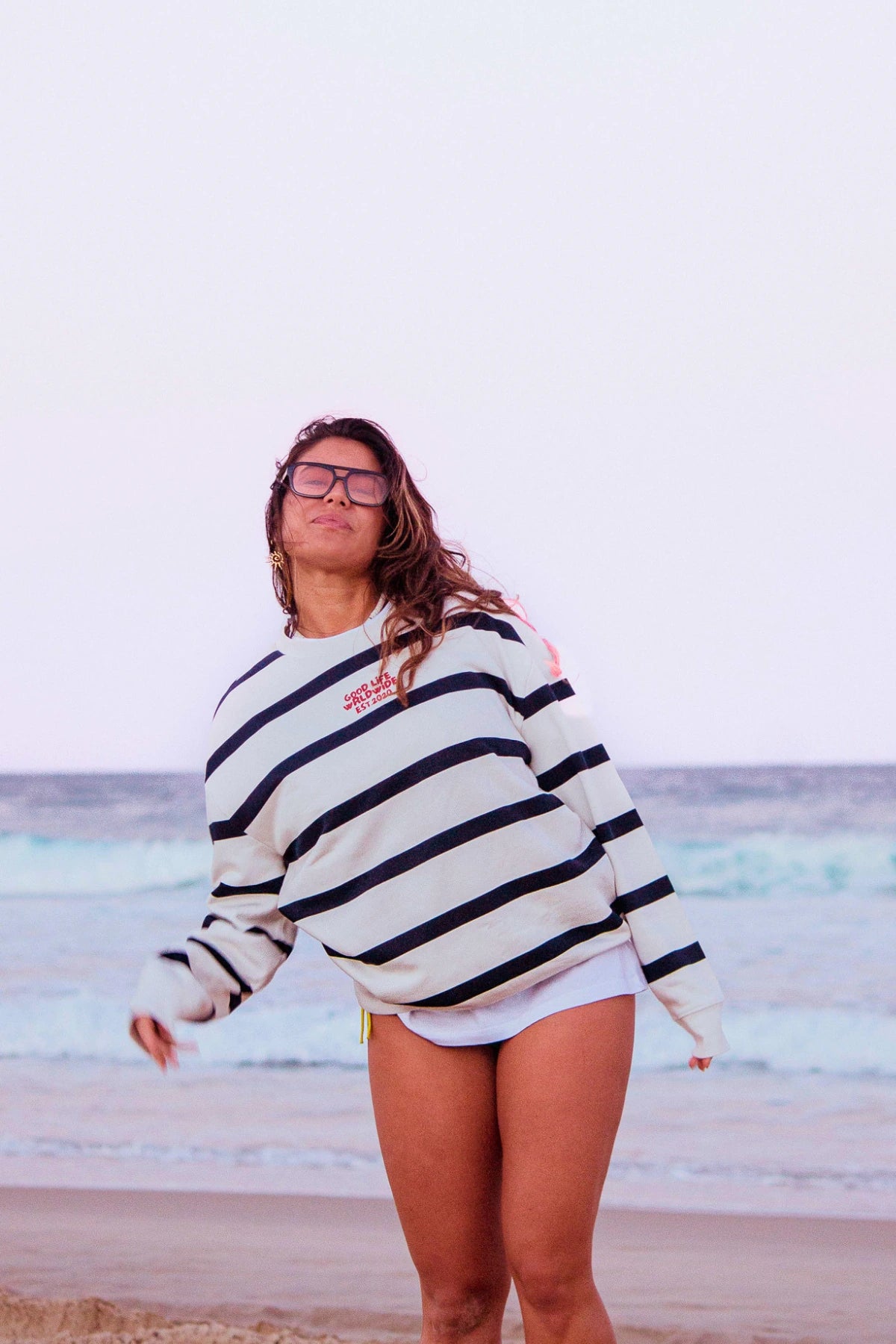 Ganzkörperaufnahme des Dockside Rebel Sweater Cream am Strand mit Meerblick und lässigem Küsten-Look.