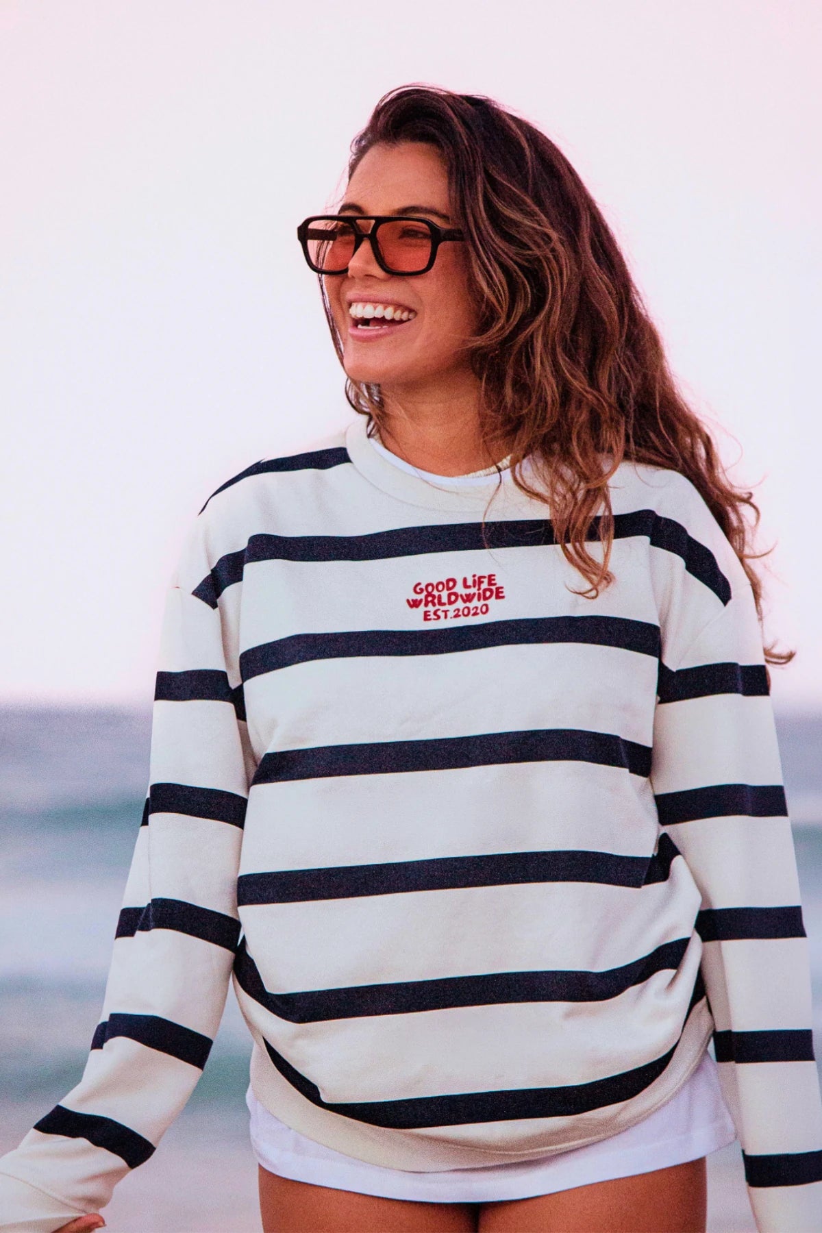 Frau im Dockside Rebel Sweater Cream mit maritimen Streifen am Strand vor dem Meer in entspannter Lifestyle-Atmosphäre.