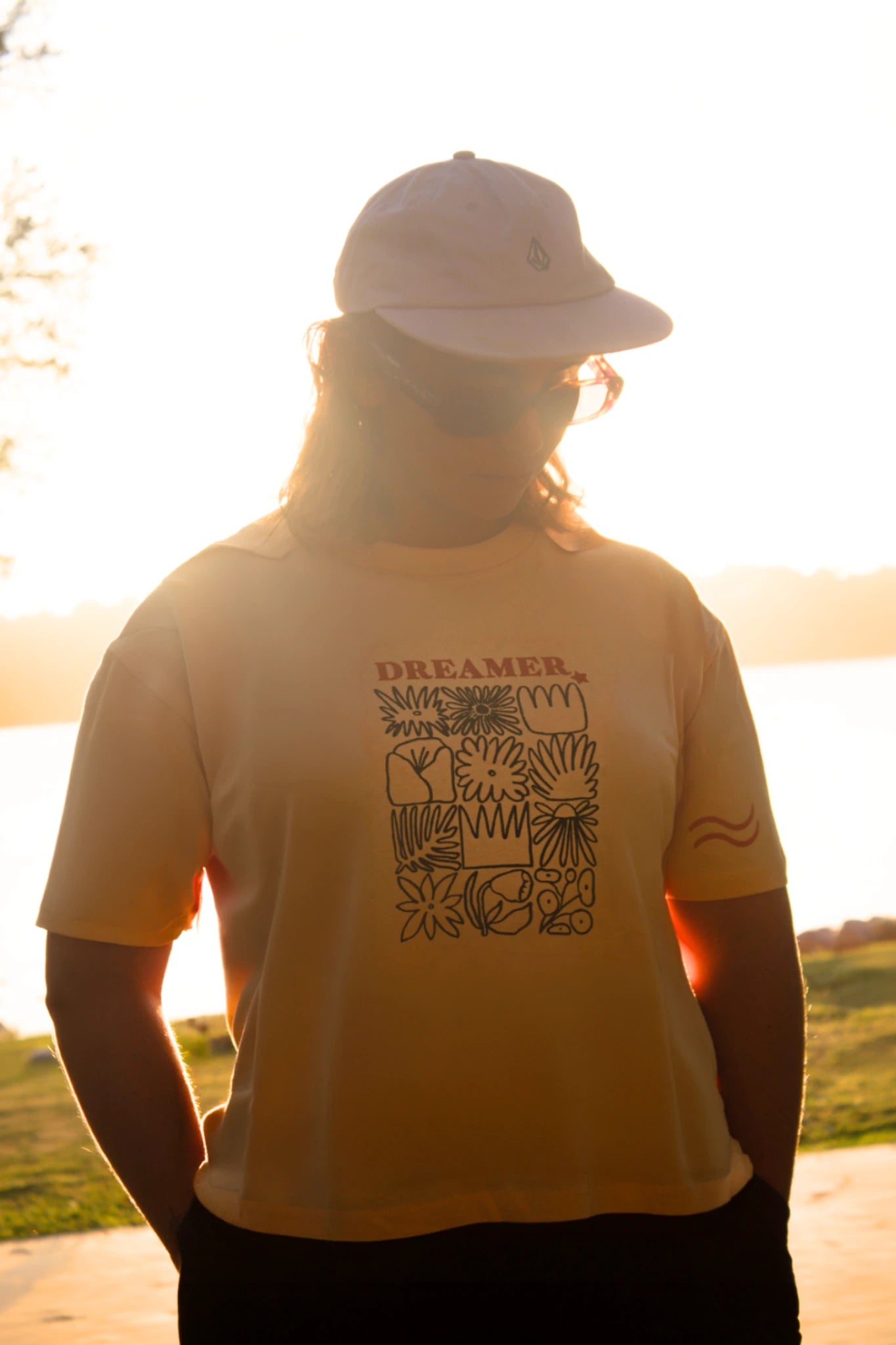 Person trägt papayafarbenes Dreamer T-Shirt mit Frontprint bei Sonnenuntergang am See