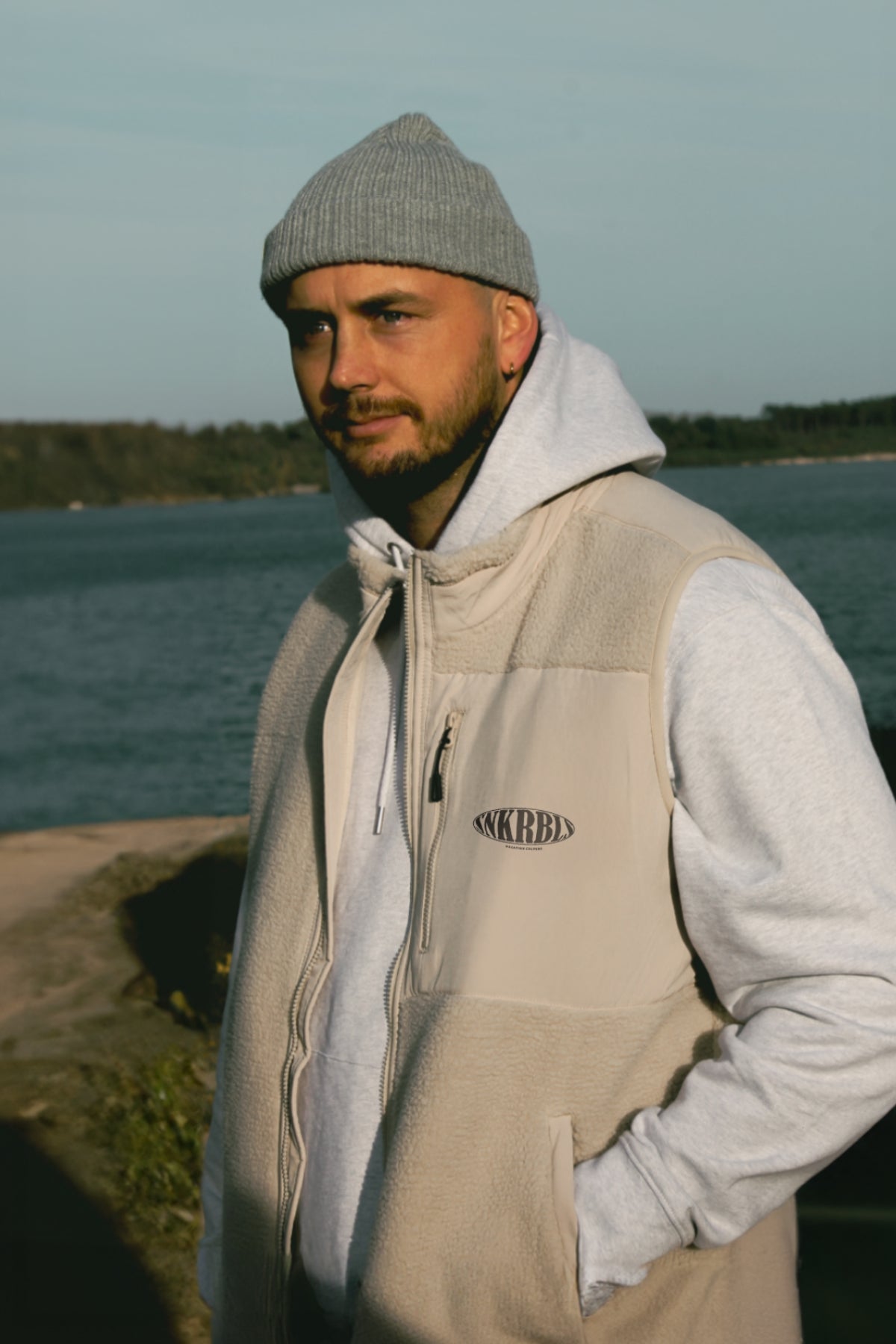 Manmn steht am strand und trägt Beanie und Fleece Weste