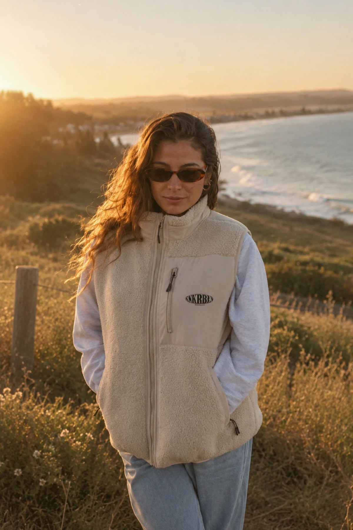 Entspannter Coastal Style mit beigefarbener Fleece-Weste von The Sunkissed Rebels kombiniert mit grauem Pullover und Jeans.