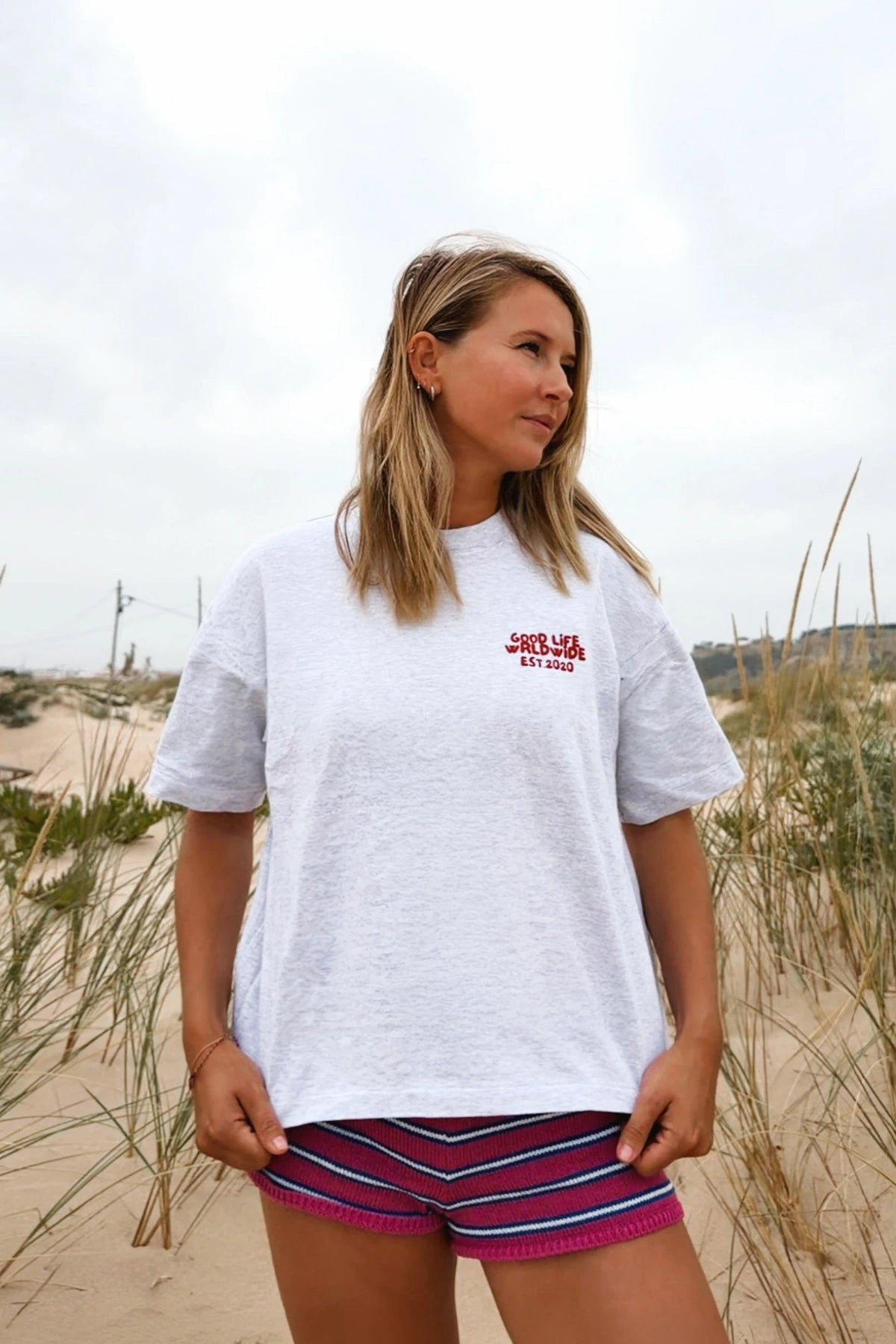 Frau trägt das Goodlife Heavy T-Shirt in Cool Grey am Strand zwischen Dünen und Strandgras.