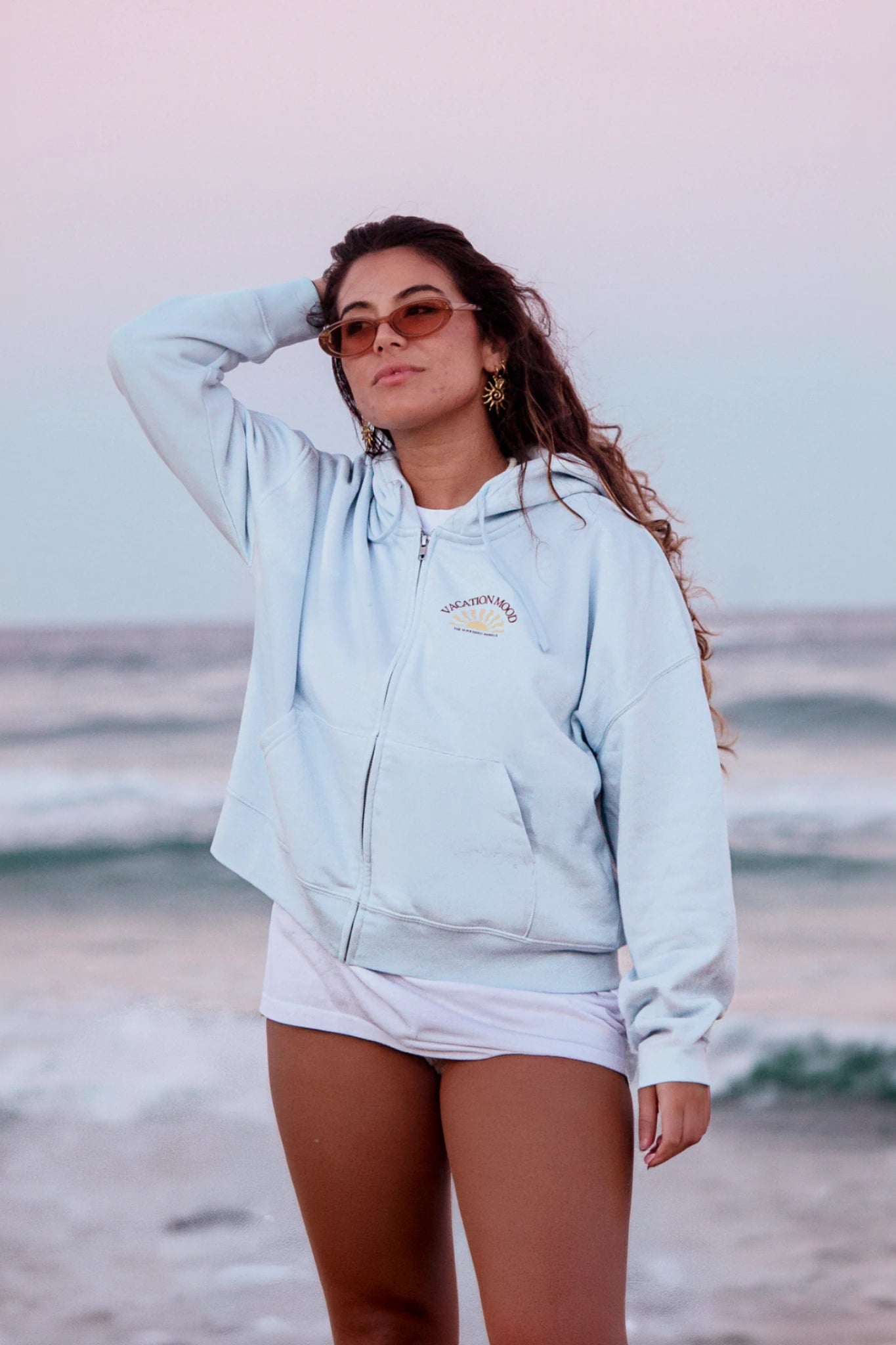 Frau am Strand trägt Iconic Women Zip Hoodie Pacific Chill im entspannten Sommer Look
