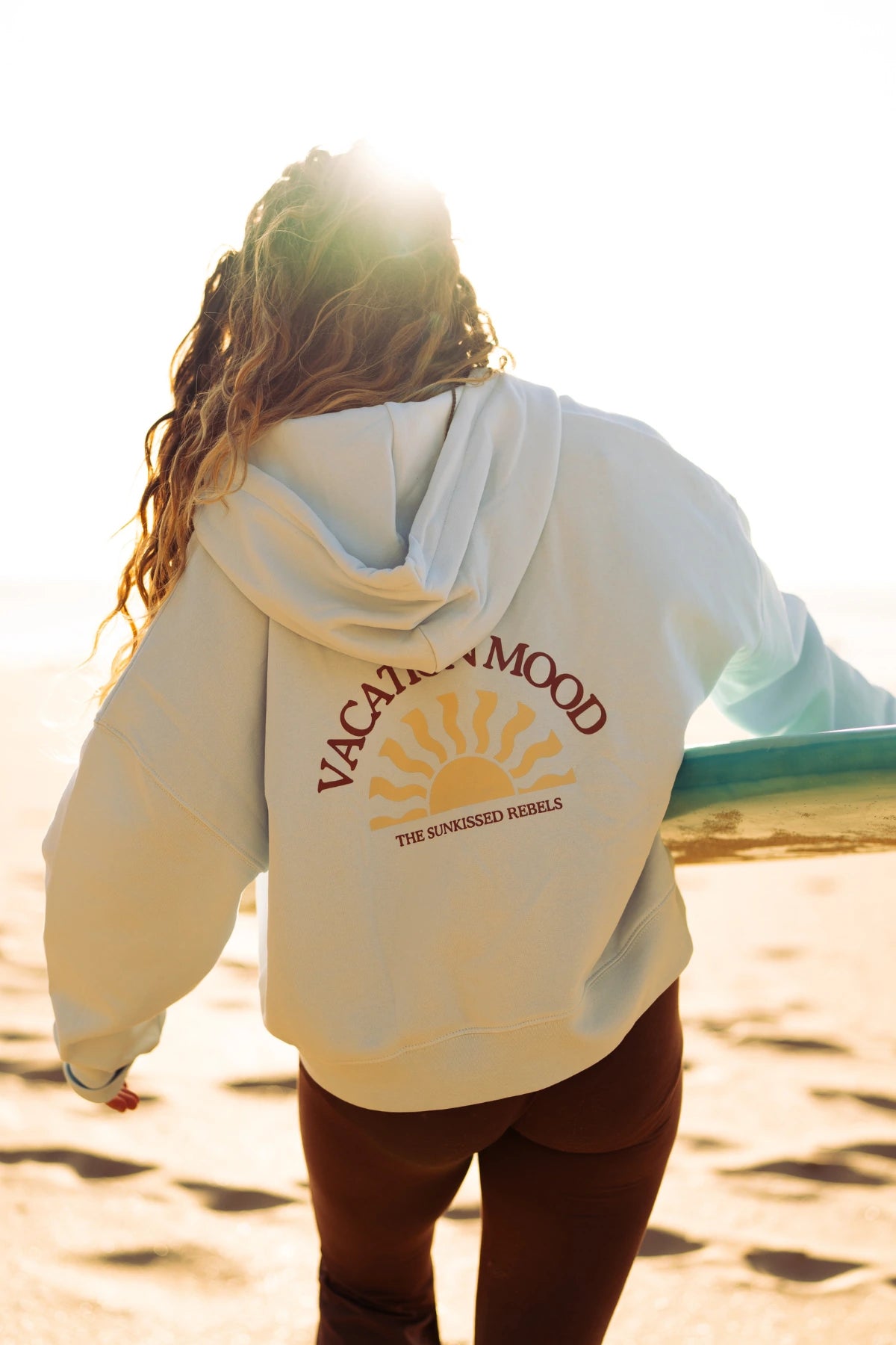 Rückenansicht des Iconic Women Zip-Hoodie Pacific Chill mit großem Vacation Mood Print und Surfboard am Strand.
