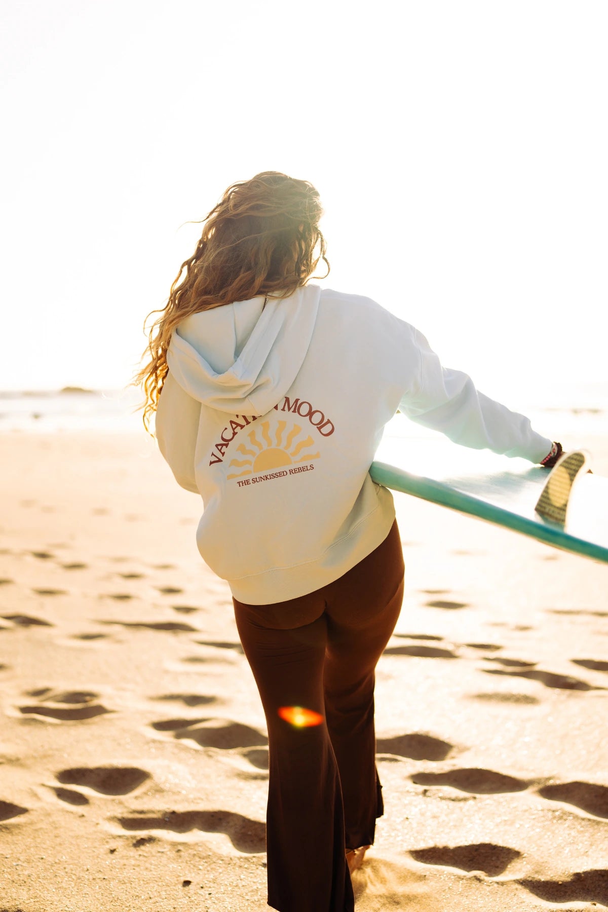 Rückenansicht des Iconic Women Zip-Hoodie Pacific Chill mit großem Vacation Mood Rückenprint am sonnigen Strand.