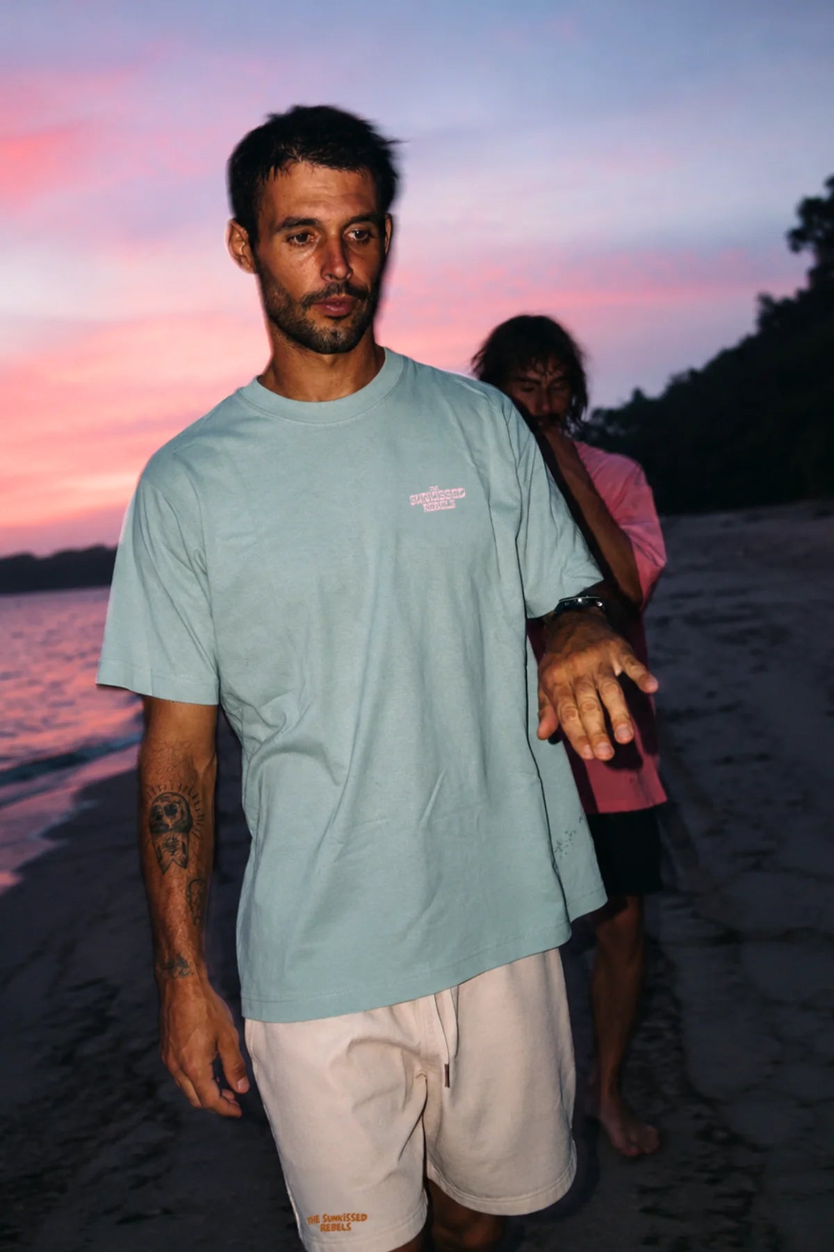 Mann trägt das hellgrüne Live Free Oversized T-Shirt mit Stickerei am Strand während der Dämmerung.