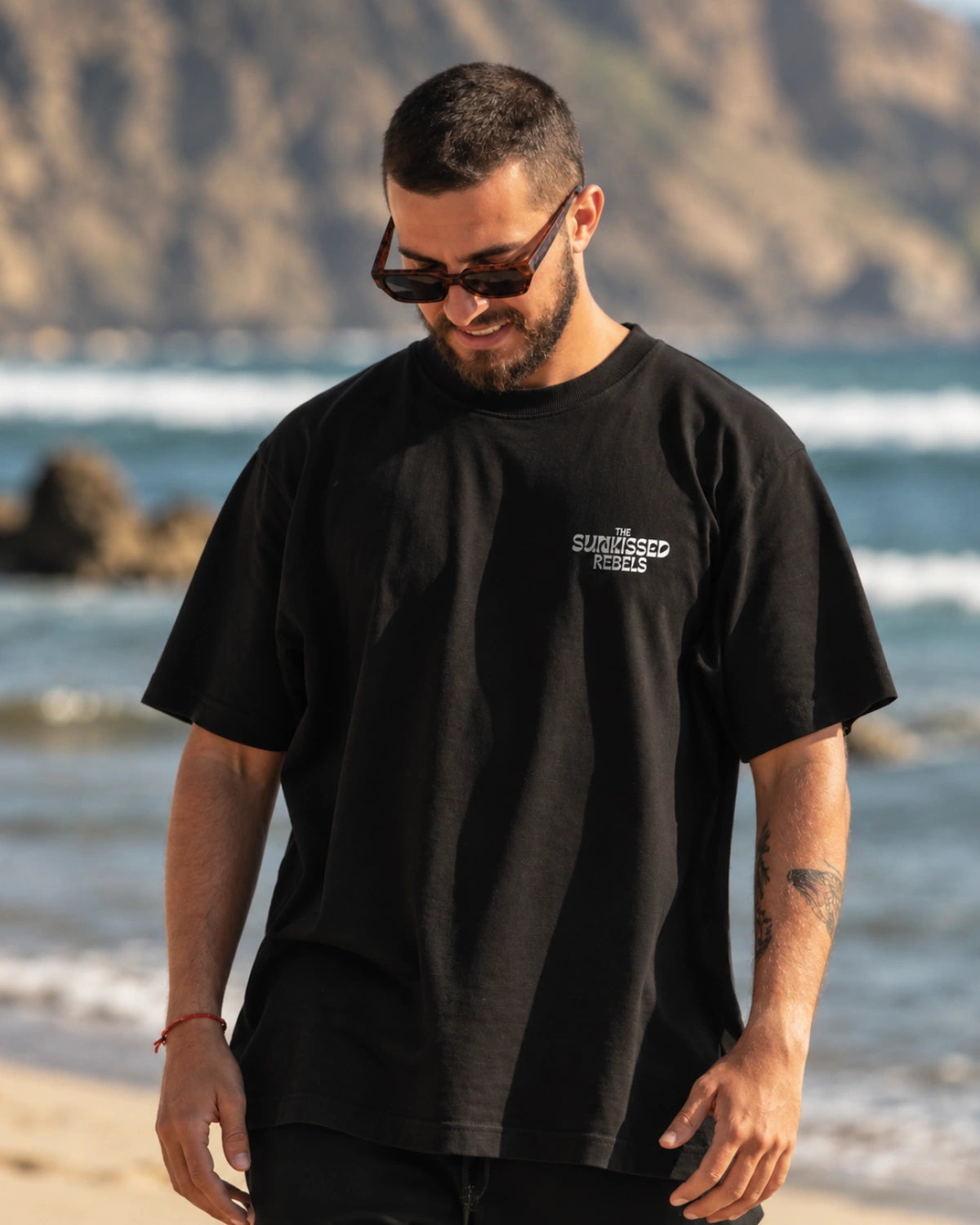 Schwarzes Live Free Oversized T-Shirt von The Sunkissed Rebels mit kleinem Logo auf der Brust am Strand