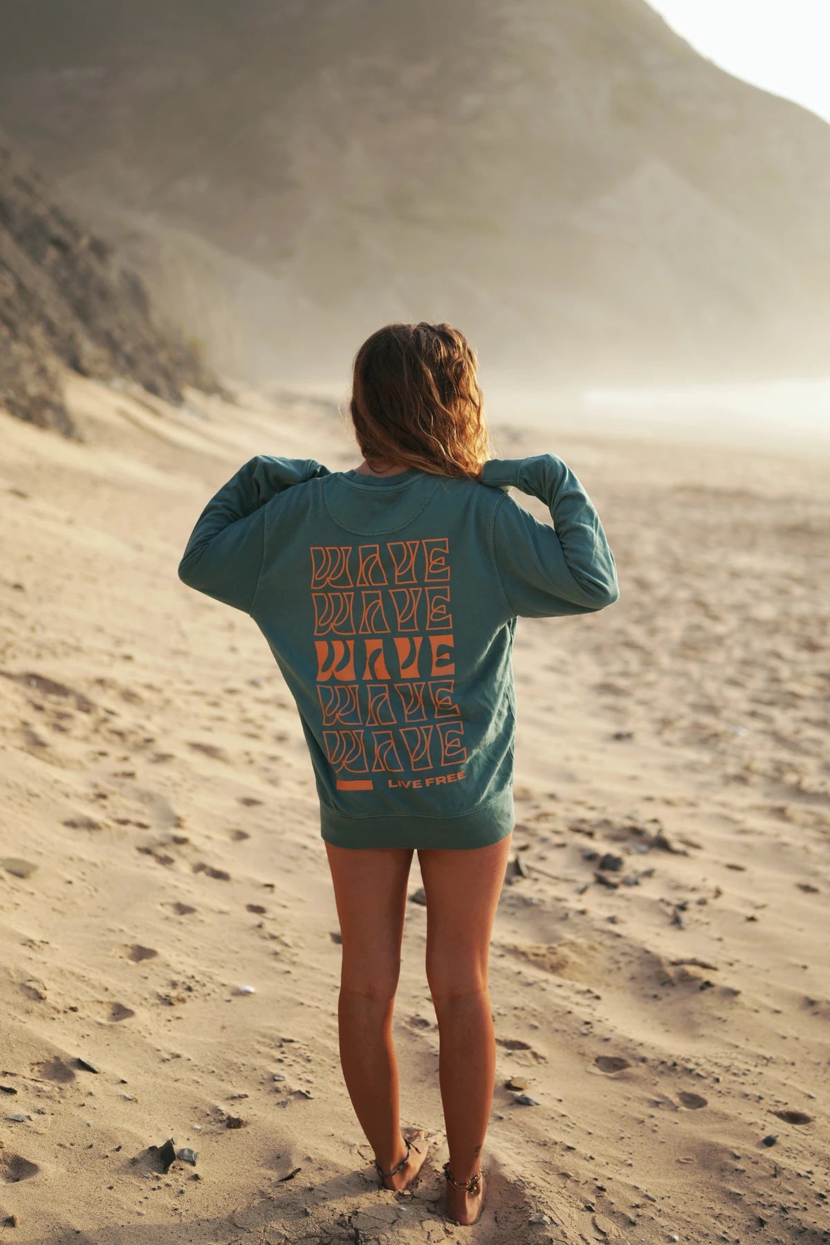  Rückseite des grünen Live Free Sweaters mit WAVE-Print am Sandstrand