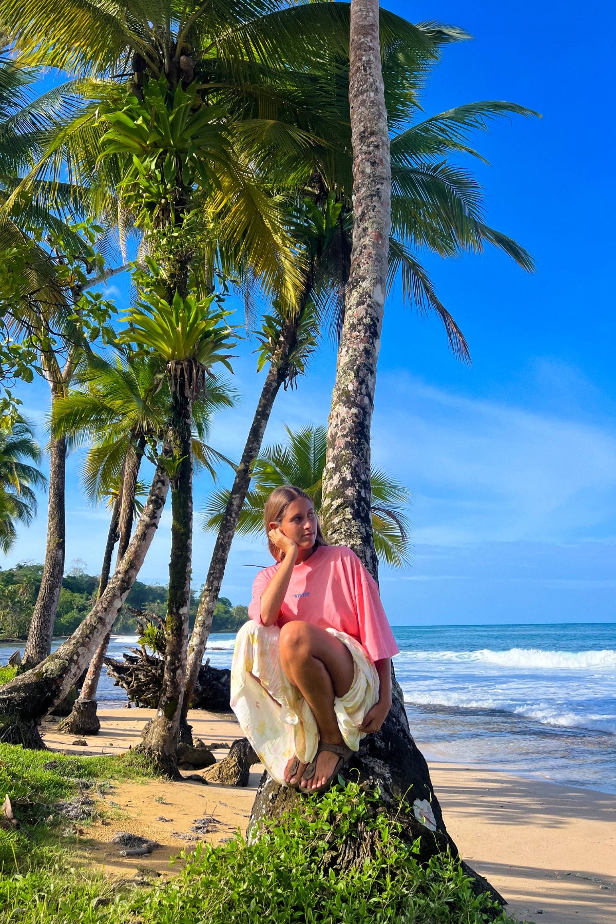 Frau trägt das Pink Joy No Bullshit Whale Boxy Oversized T-Shirt an einem tropischen Strand mit Palmen und Meer.