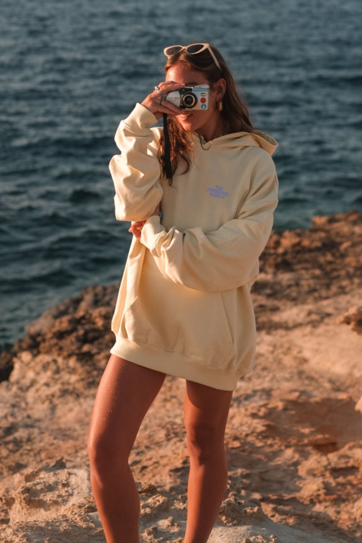 Frau trägt A Good Day Hoodie in butter am Strand un macht ein Foto. 