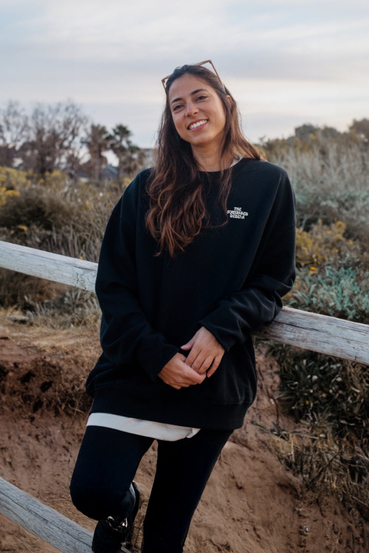 Frau trägt schwarzen Oversized Sweater von The Sunkissed Rebels am Strand. 