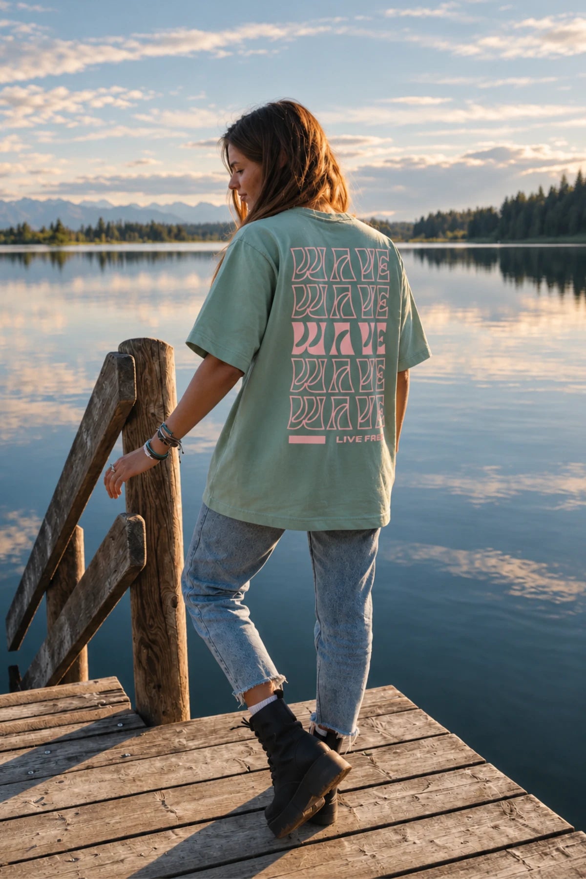 Rückansicht des Live Free Oversized Shirts in Aloe kombiniert mit Jeans und Boots am See – The Sunkissed Rebels
