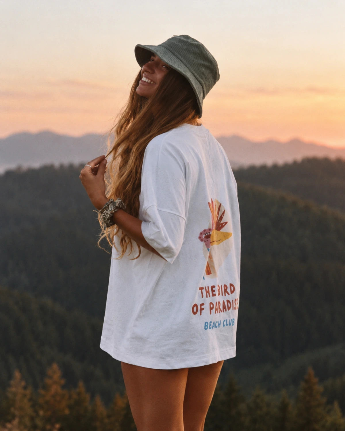Frau trägt das Bird of Paradise Oversized T-Shirt in White mit großem Bird of Paradise Rückenprint in den Bergen