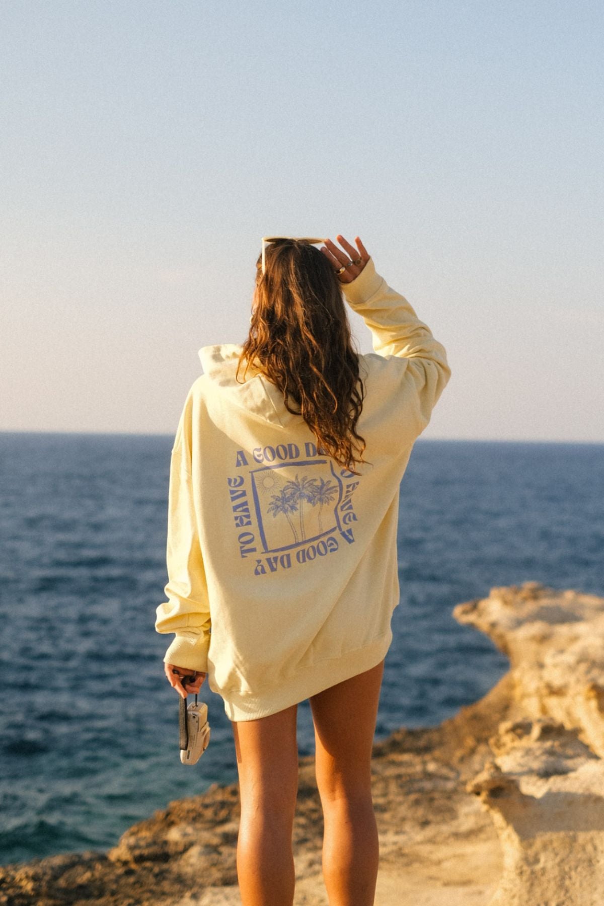 Frau trägt Oversized Hoodie in butter von The Sunkissed Rebels am Strand. 