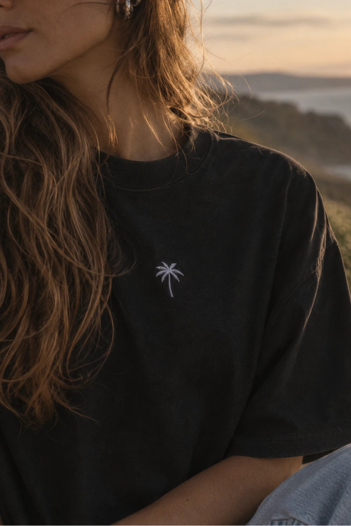 Nahaufnahme der weißen Palmen-Stickerei auf der Brust des schwarzen Palm Tree Boxy Oversized T-Shirts von The Sunkissed Rebels.