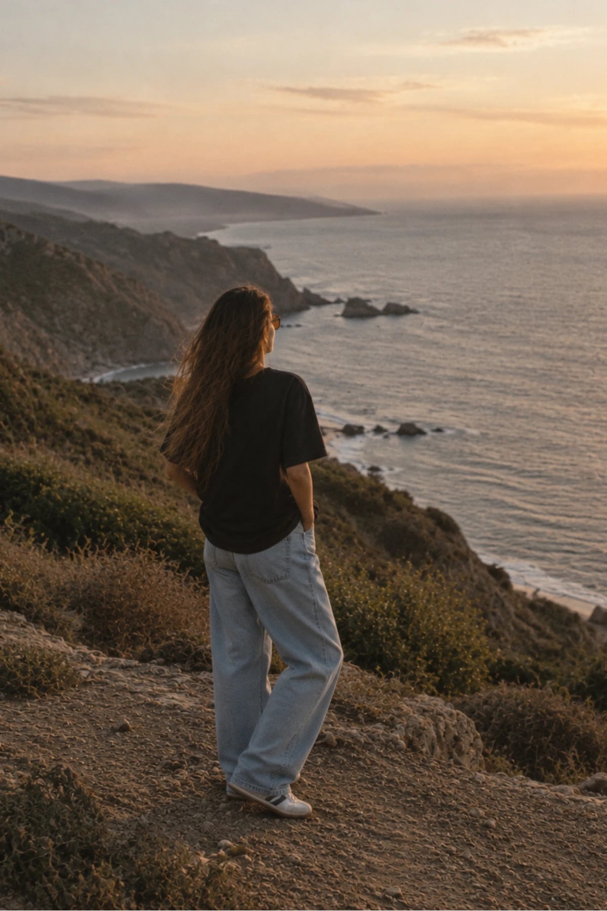Rückenansicht des schwarzen Oversized Shirts von The Sunkissed Rebels im warmen Sonnenuntergang an den Klippen.