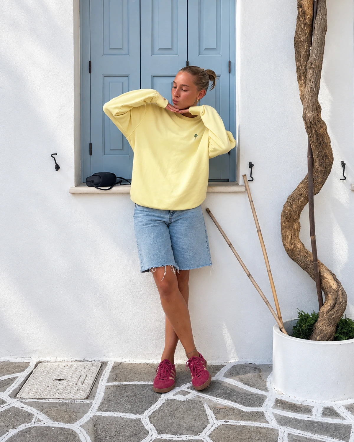 Frau im Palm Tree Sweater in Butter mit Jeansshorts und pinken Sneakern im sommerlichen Lifestyle Look