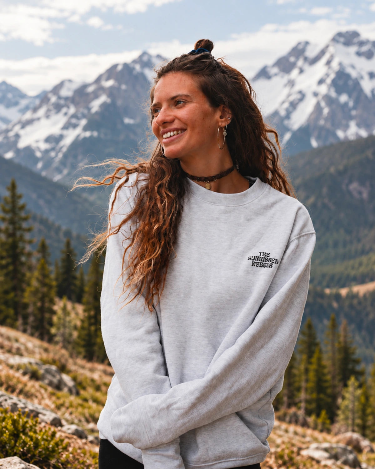 Frau trägt den Paradise & Sunset Sweater in Cool Grey von The Sunkissed Rebels vor einer Bergkulisse