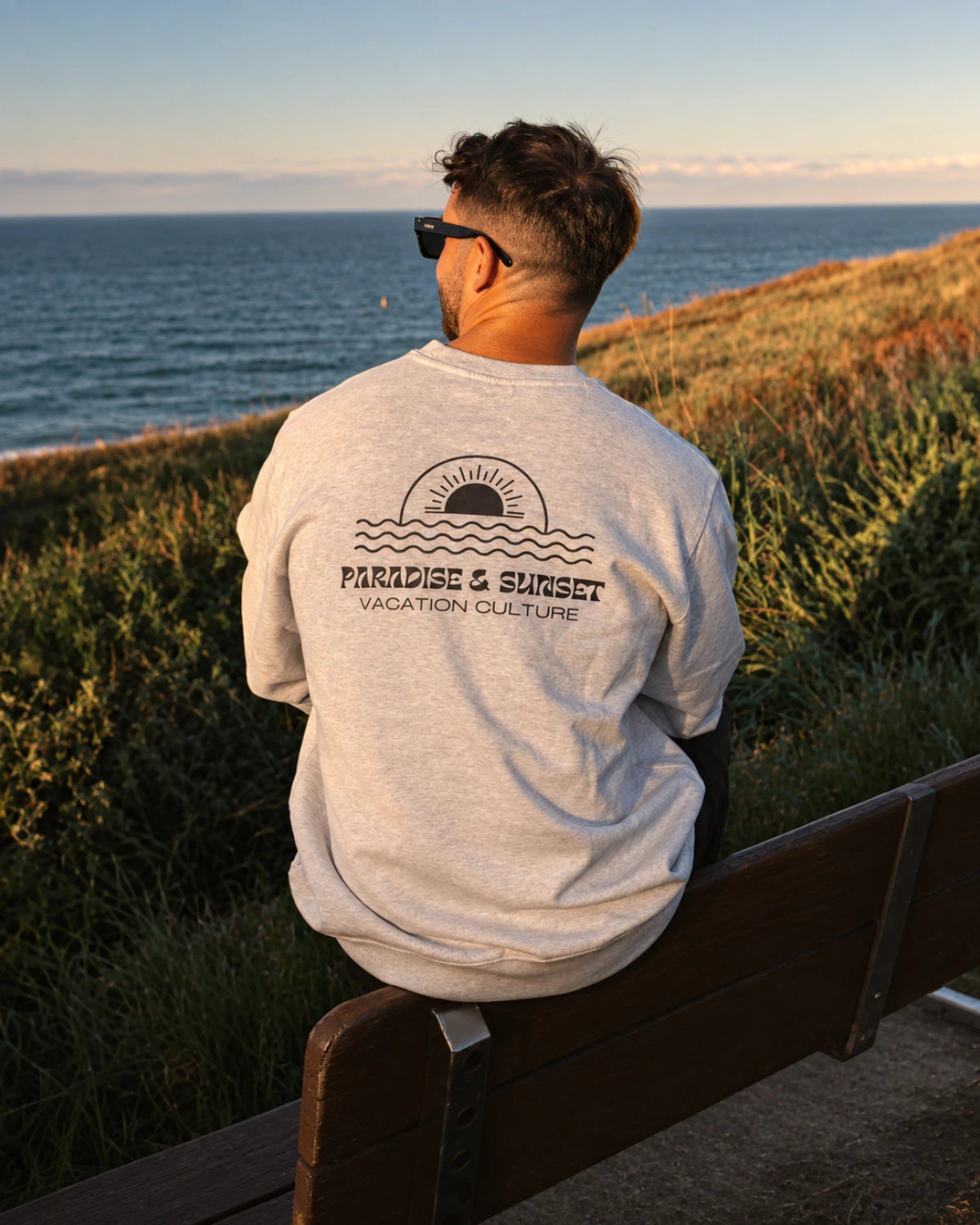 Mann trägt den Paradise & Sunset Sweater in Cool Grey mit  
Rückenprint