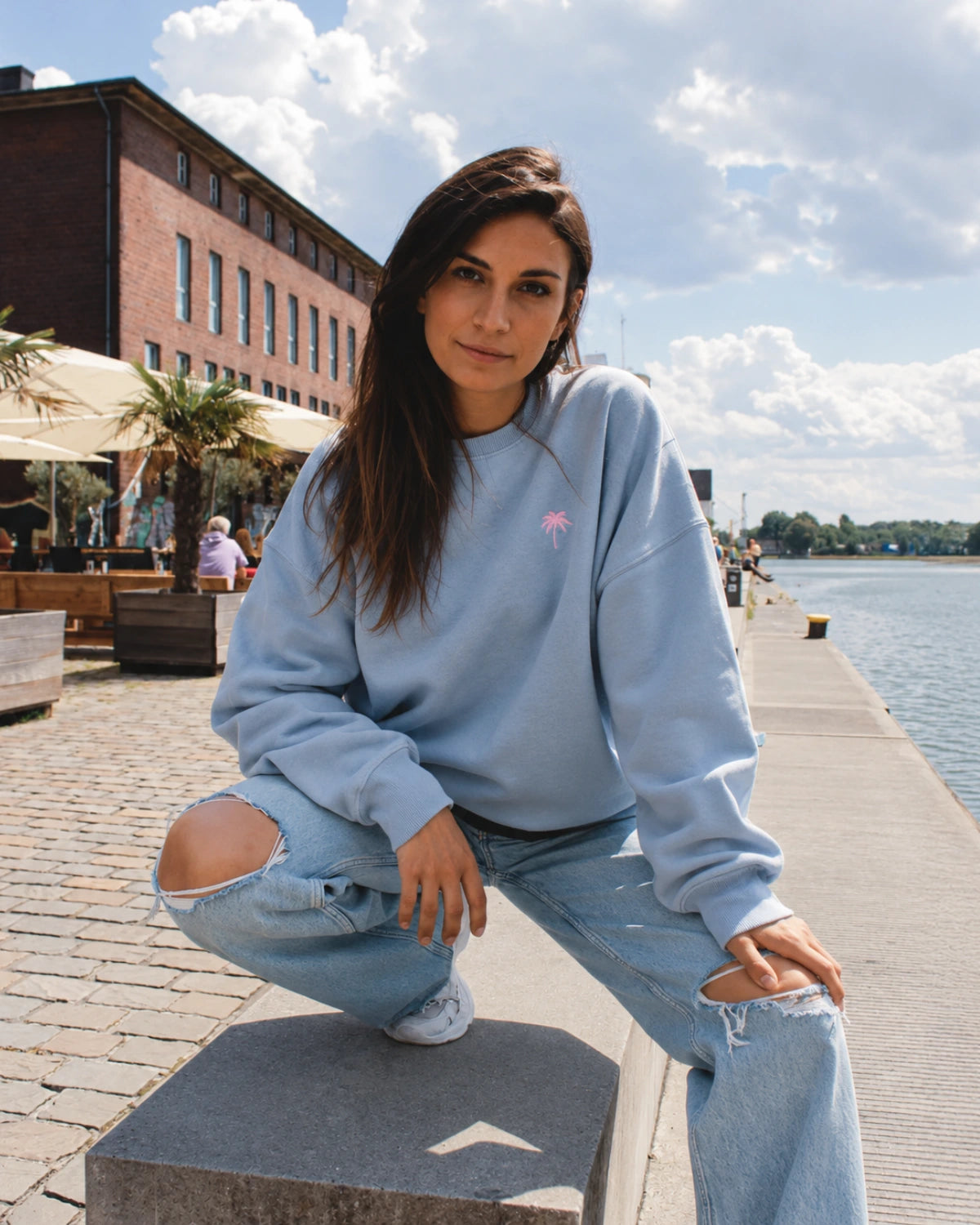 Frau trägt den Pink Palm Oversized Vintage Sweater in Serene Blue von The Sunkissed Rebels am Hafen