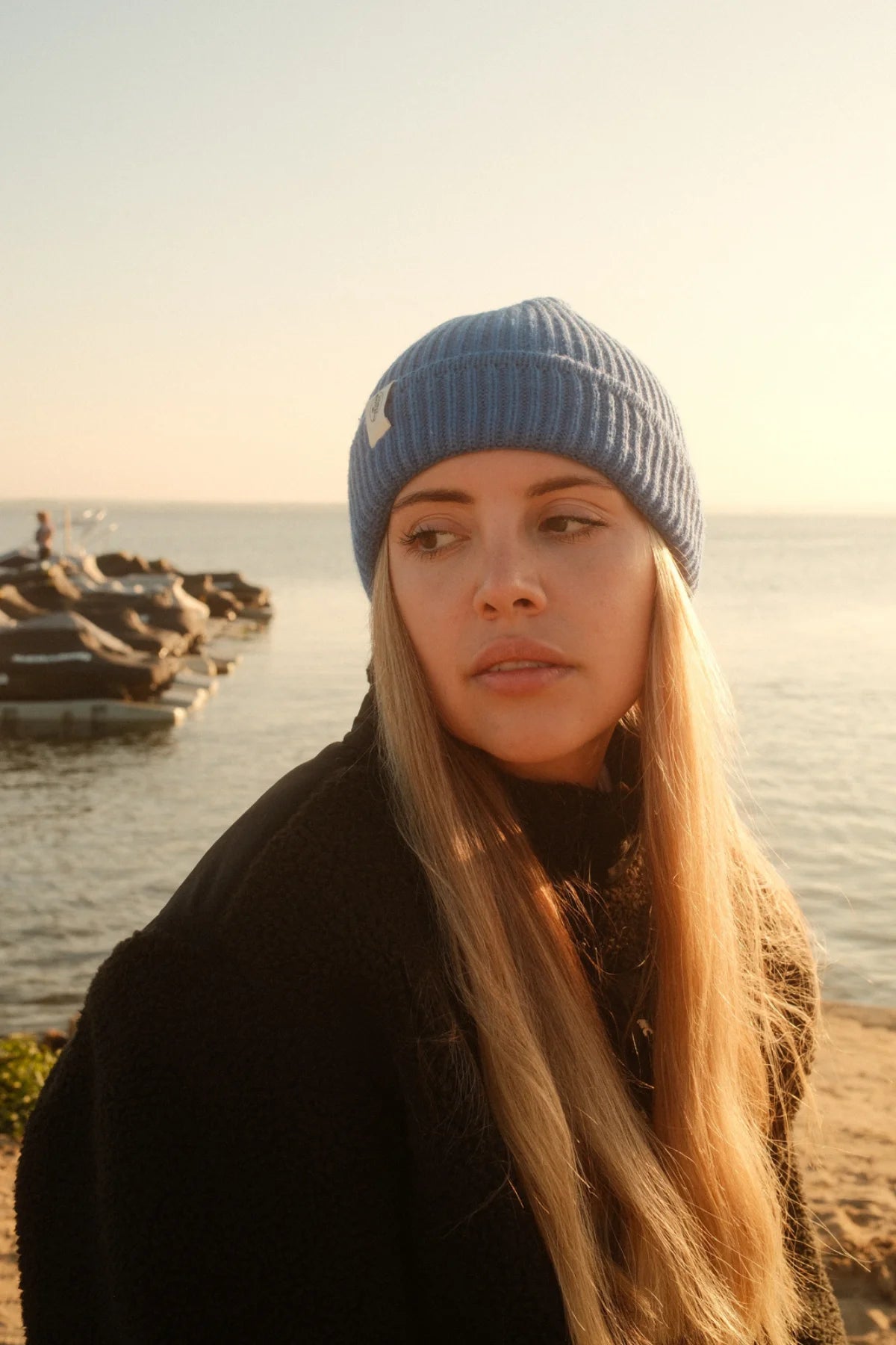 Frau am Strand mit blauer Strickmütze Rebels Knit Beanie in Ocean Blue von The Sunkissed Rebels mit Label-Patch.