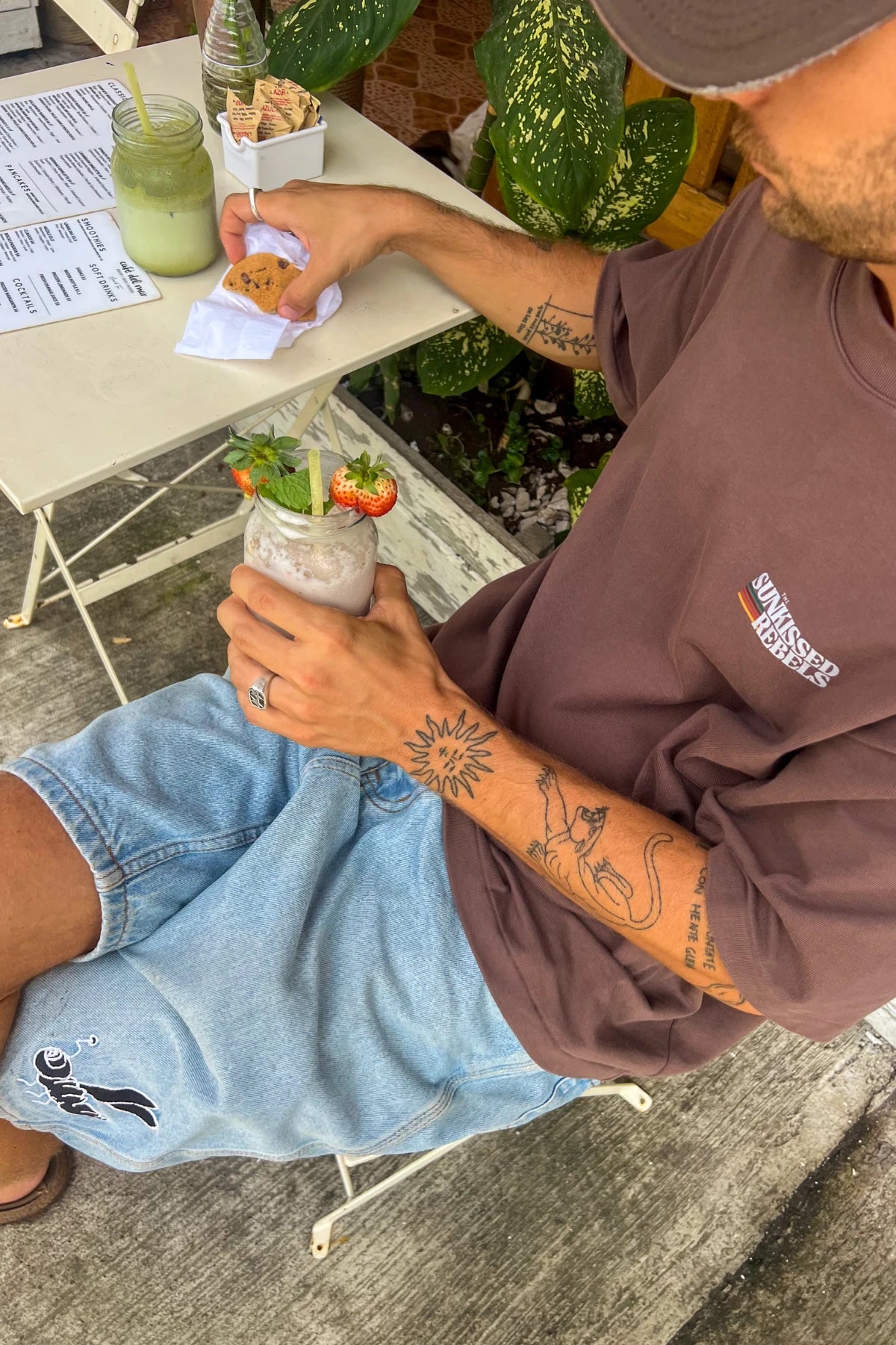 Mann trägt das Retro Vibes Heavy T-Shirt in Mocha mit kleinem Brustlogo in einem gemütlichen Café während des Frühstücks.