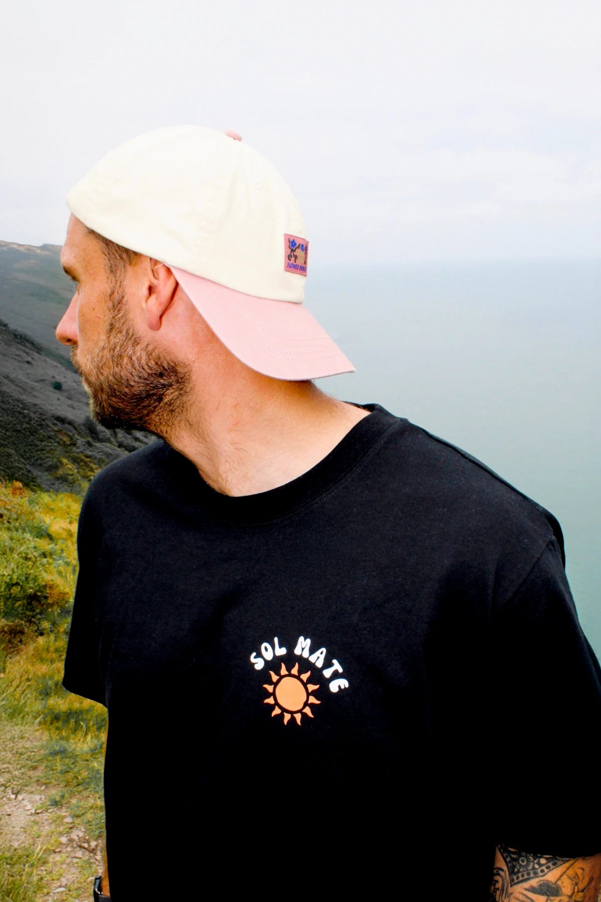 Nahaufnahme des Sol Mate Oversized T-Shirts in Schwarz mit Sonnen-Print auf der Brust, getragen in einer Küstenlandschaft.