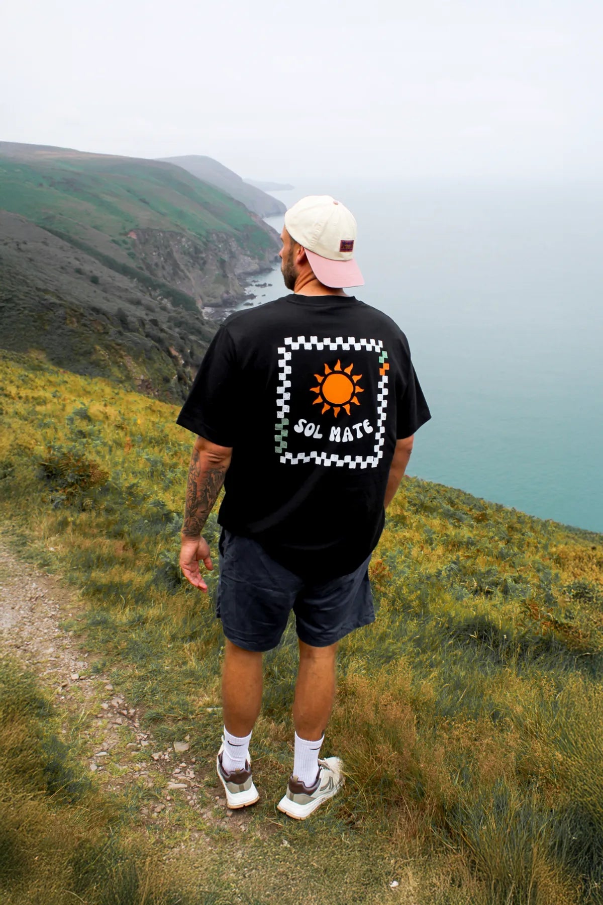 Sol Mate Oversized T-Shirt mit auffälligem Rückenprint, getragen bei einer Wanderung an der Küste.