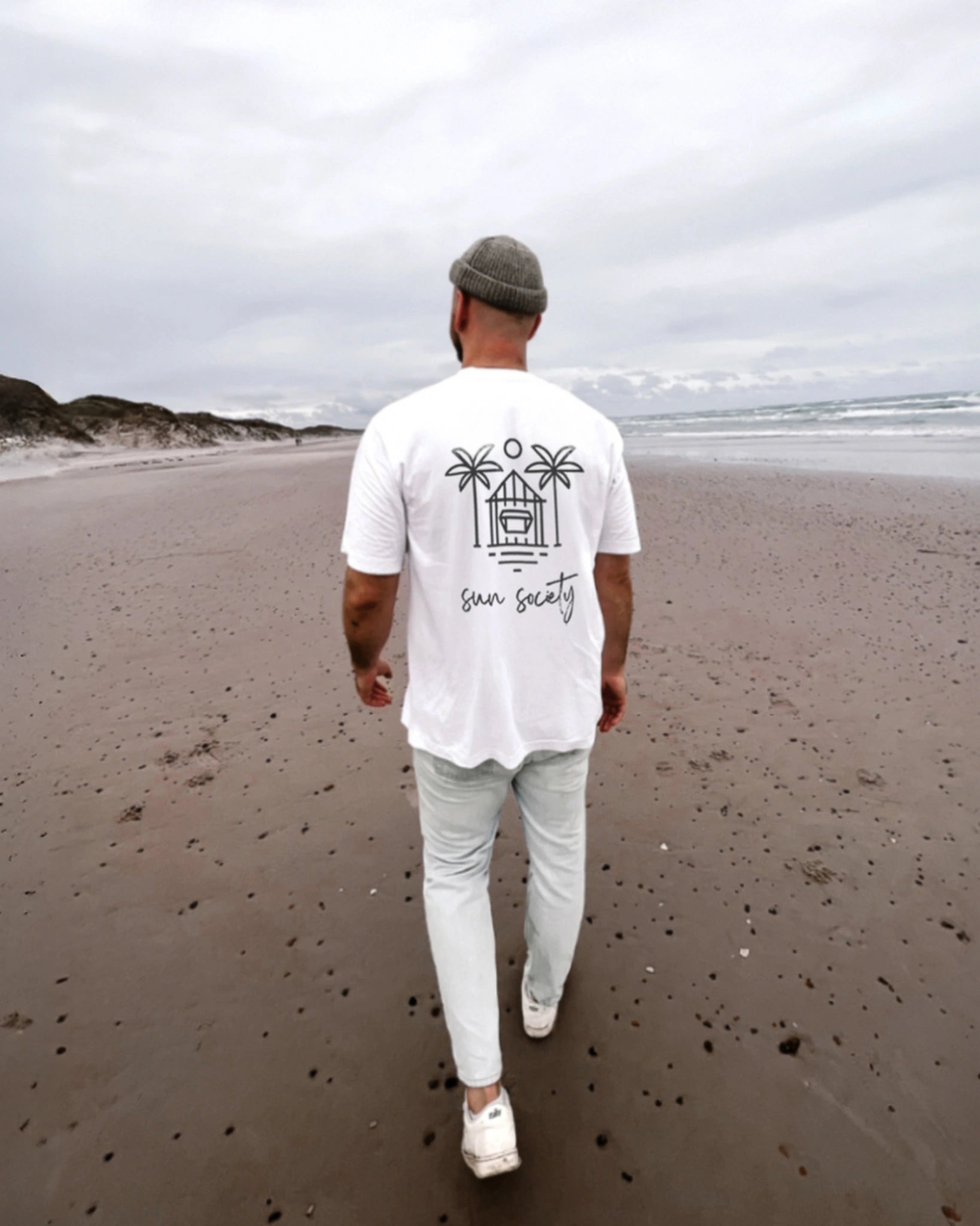 The Sunkissed Rebels Sun Society Backprint Shirt – Herren T-Shirt am Strand von hinten fotografiert, minimalistischer Palm-Print