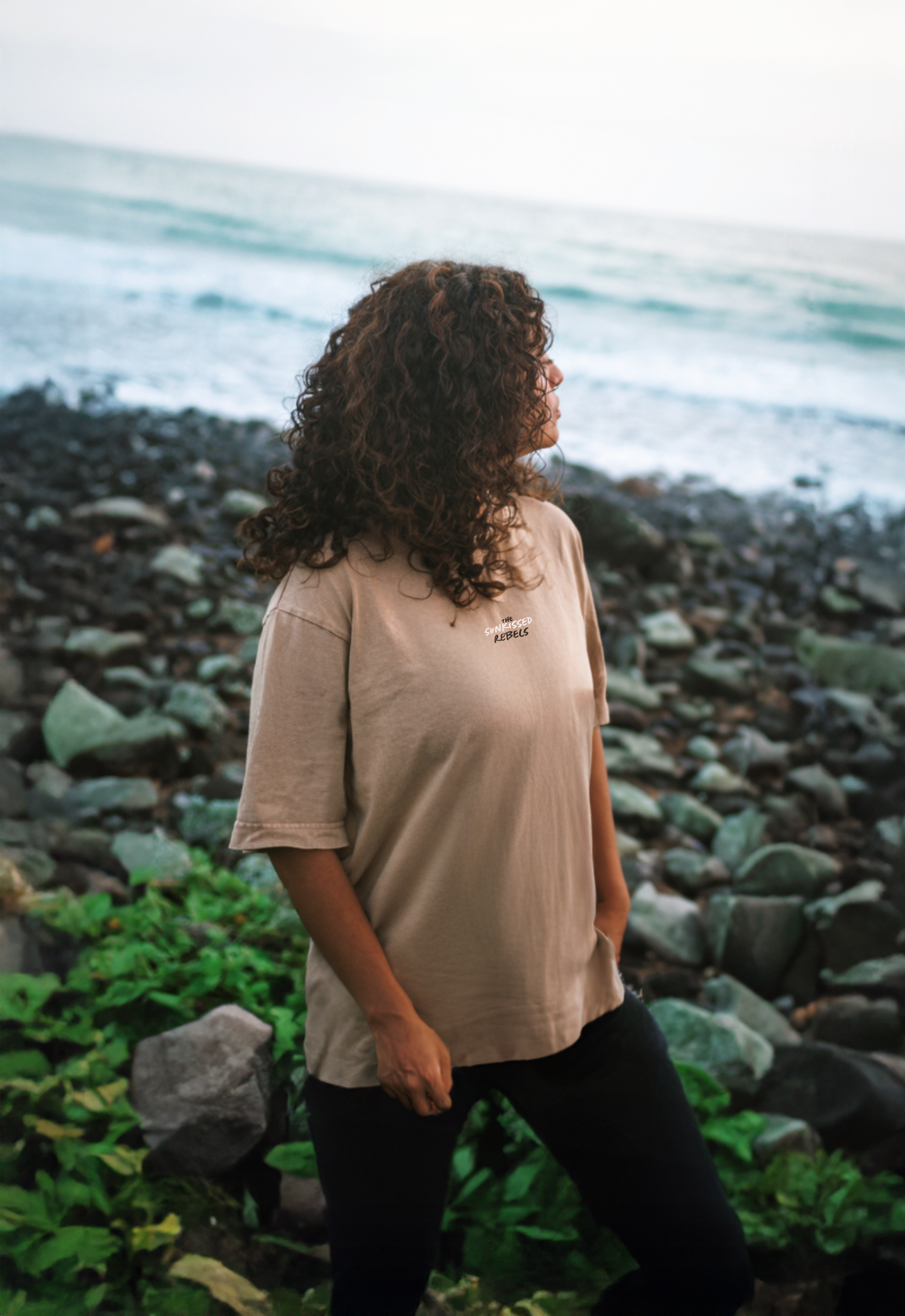 Frau trägt trägt T-Shirt mit The Sunkissed Rebels Aufschrift am Meer. 