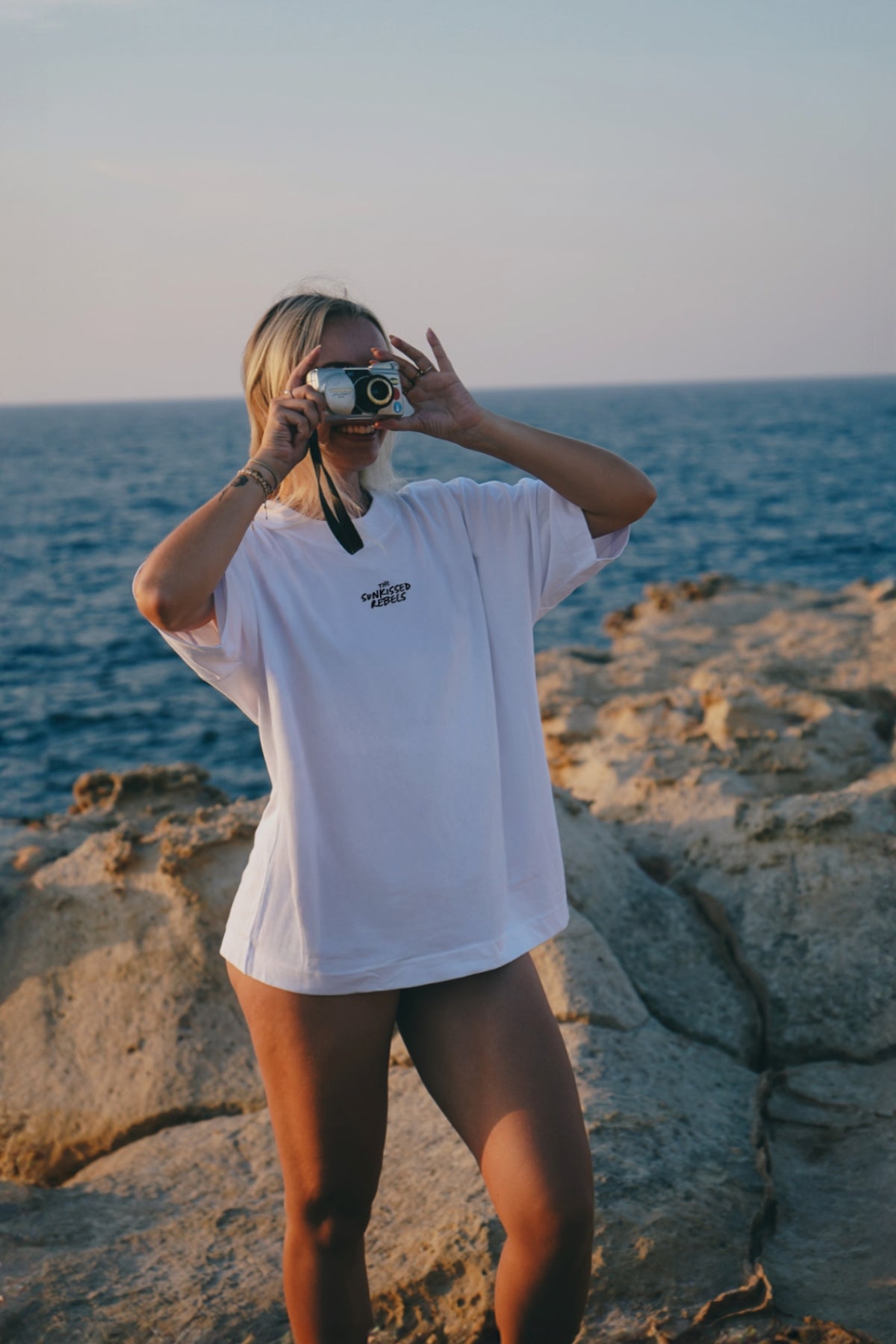 Frau mach Fotos am Strand, trägt Bikini und T-Shirt