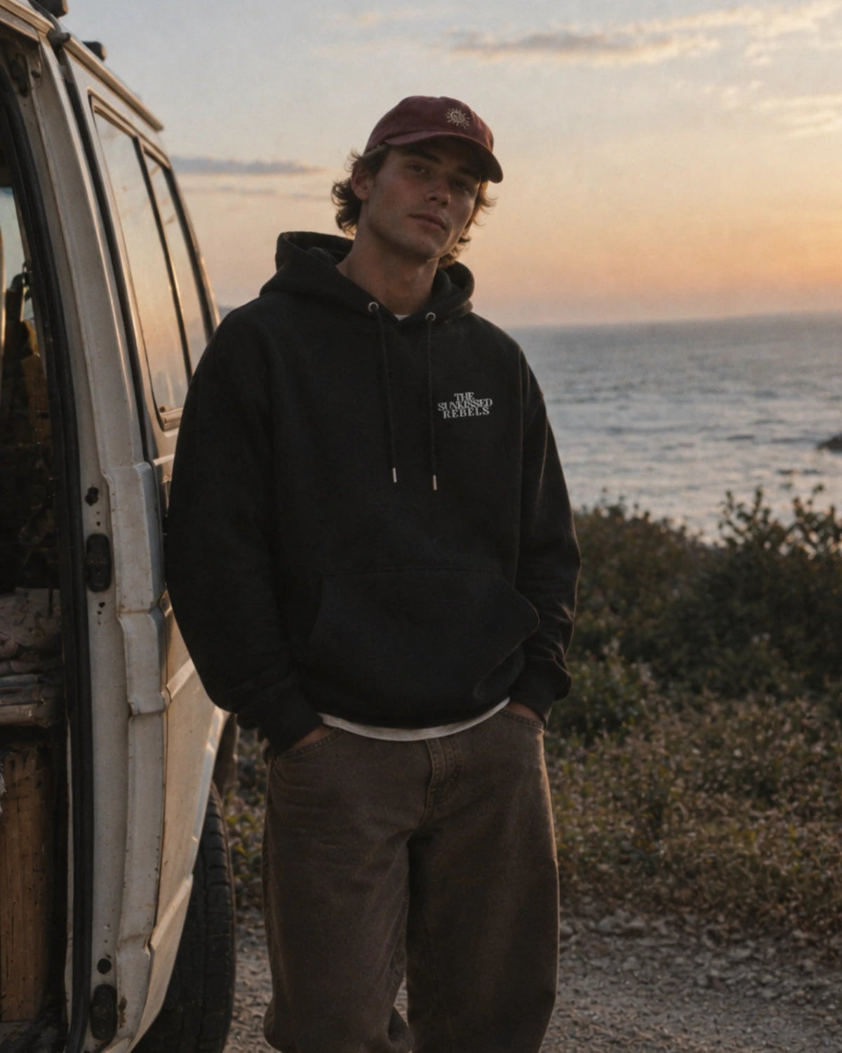 Mann im schwarzen Vacation Mood On Hoodie mit weißem Logo und roter Cap an der Steilküste