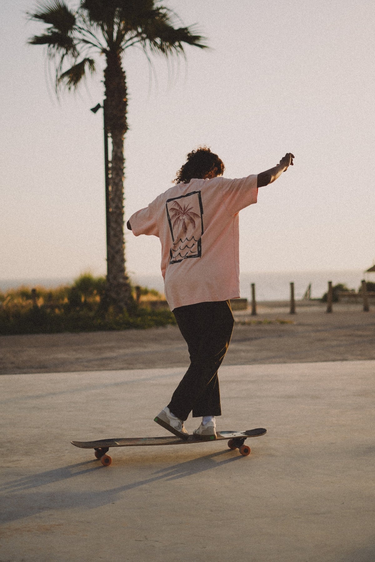 Mann im Oversized T-Shirt fährt Longboard am Strand