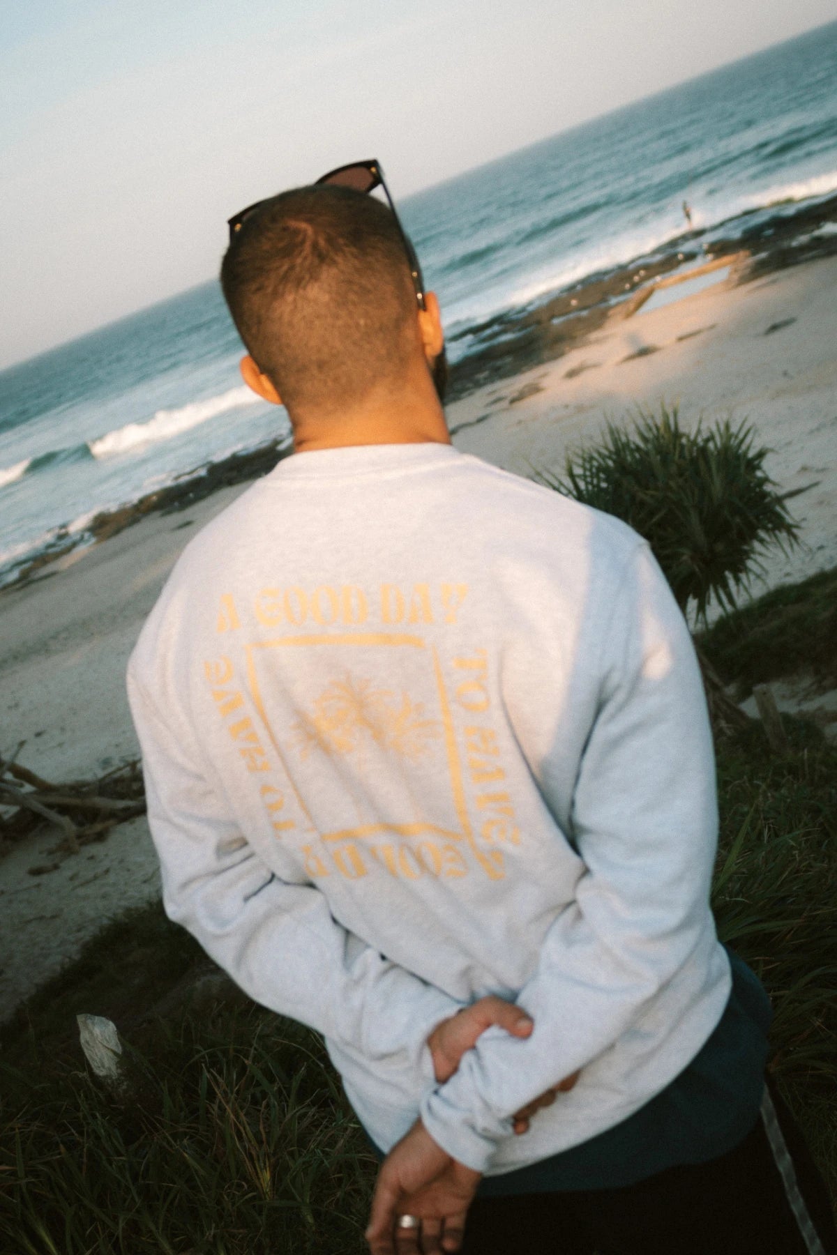 ann trägt den A Good Day Sweater in Cool Grey von The Sunkissed Rebels am Strand – entspannter Beachlook bei Sonnenuntergang.