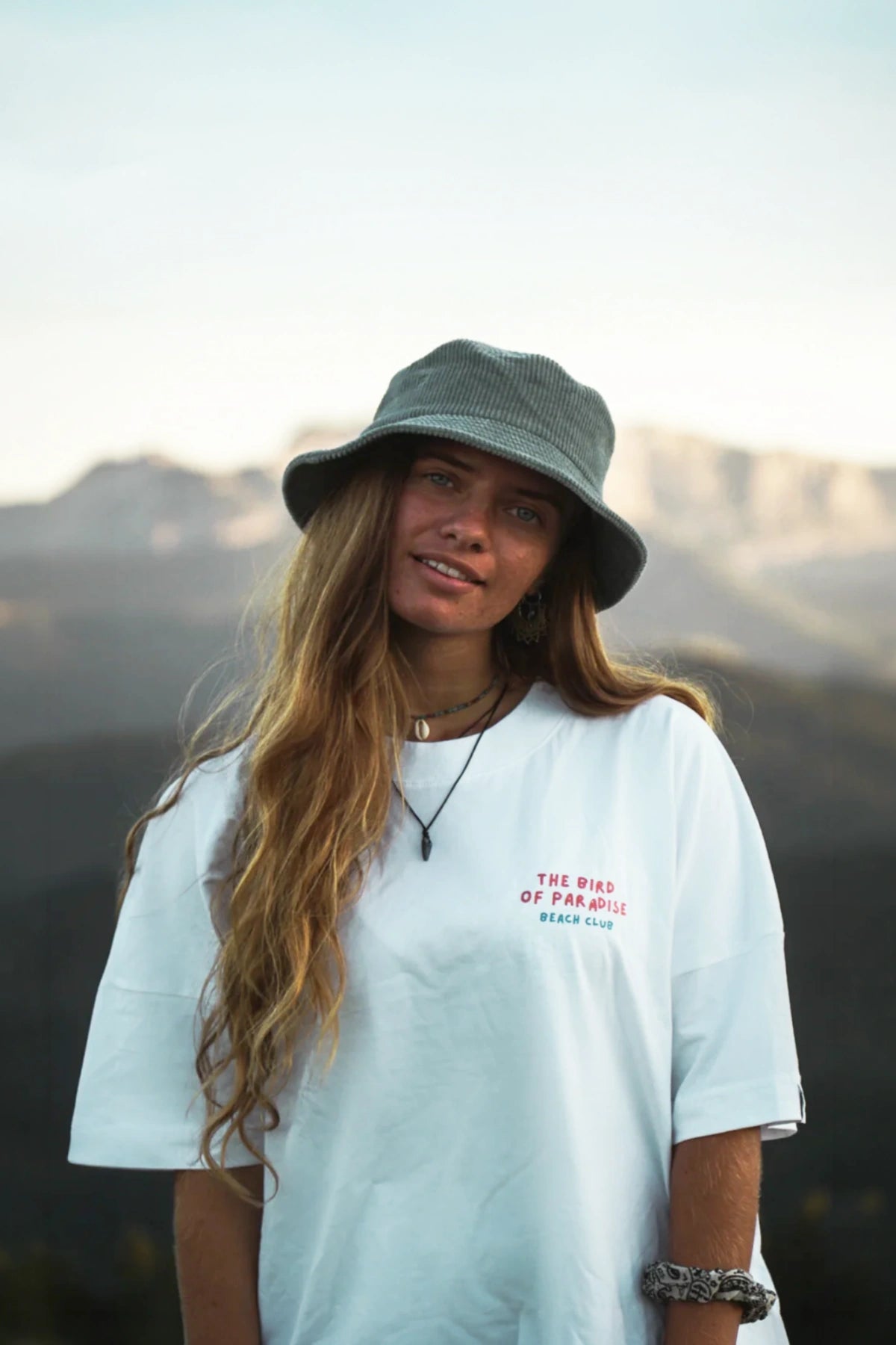 Portrait einer Frau im weißen Bird of Paradise Boxy Oversized T Shirt mit Bergkulisse und natürlichem Outdoor Look