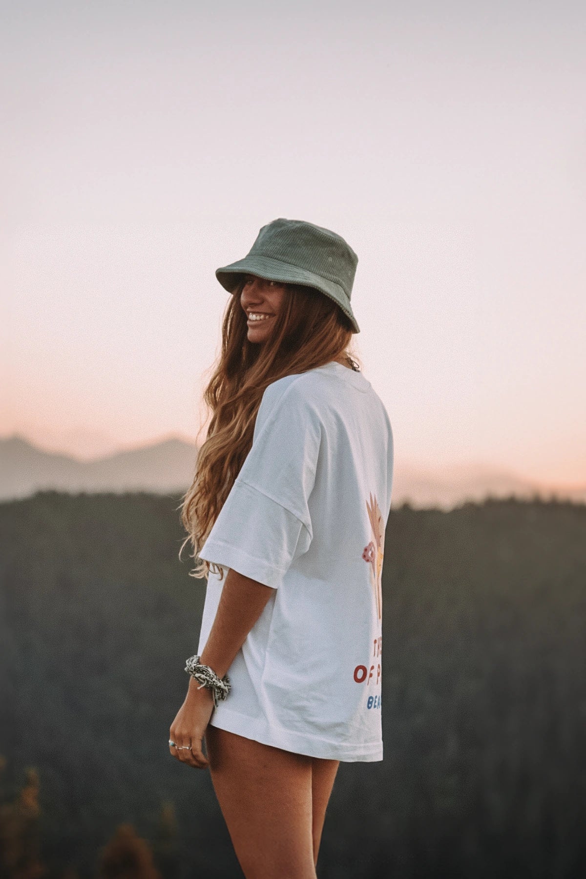 Frau trägt weißes Bird of Paradise Boxy Oversized T Shirt mit großem Backprint vor Berglandschaft im Abendlicht 