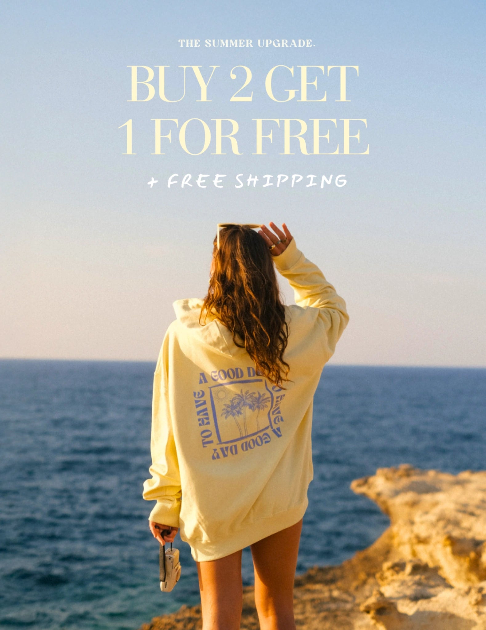 Person trägt gelben Hoodie am Meer mit Blick auf Ozean, sommerliche Promotion Buy 2 Get 1 Free, entspannter Coastal Lifestyle
