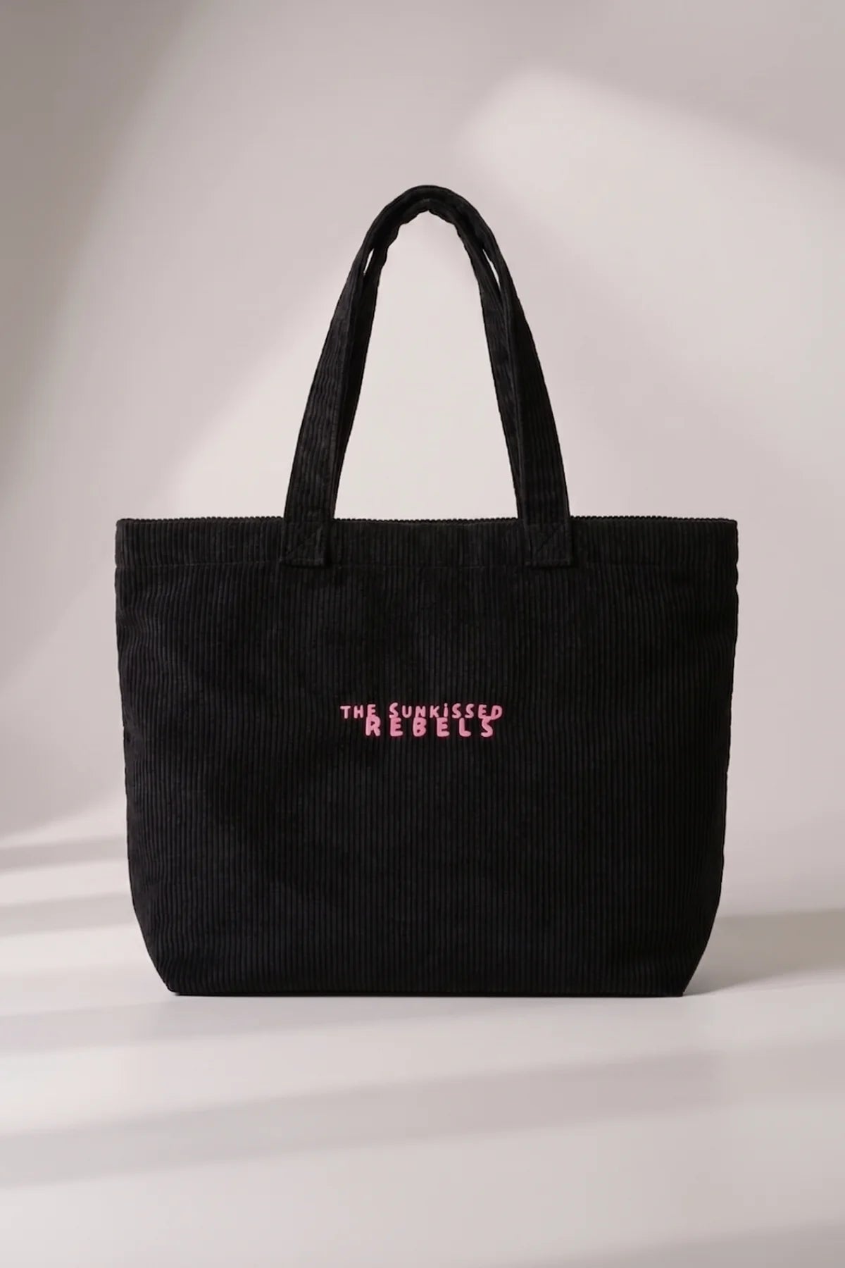 Frontansicht der schwarzen Cord Bag aus Bio-Feincord mit pink gesticktem Schriftzug "The Sunkissed Rebels".