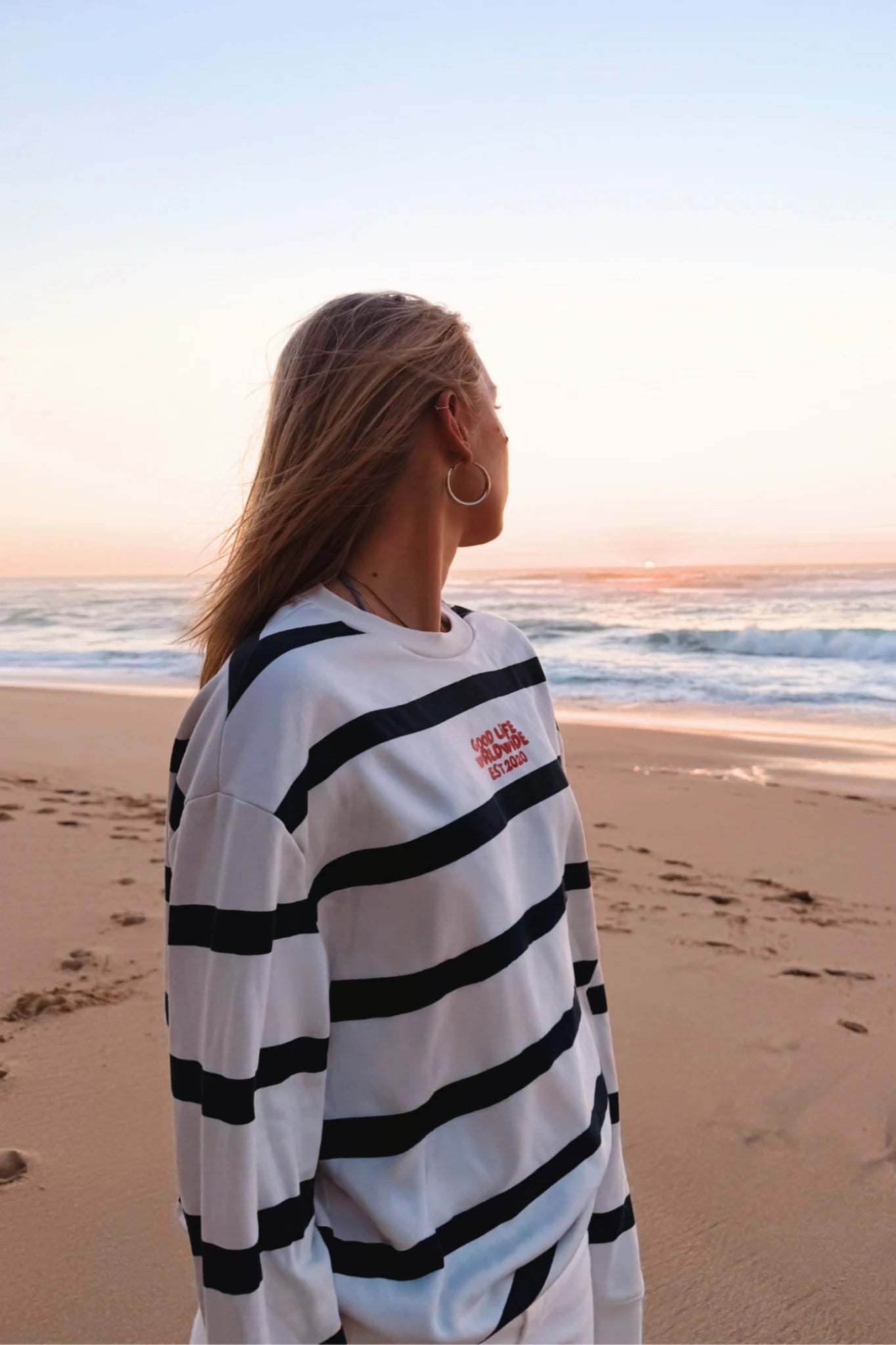 Frau trägt Dockside Rebel Sweater Vintage Cream am Strand bei Sonnenuntergang