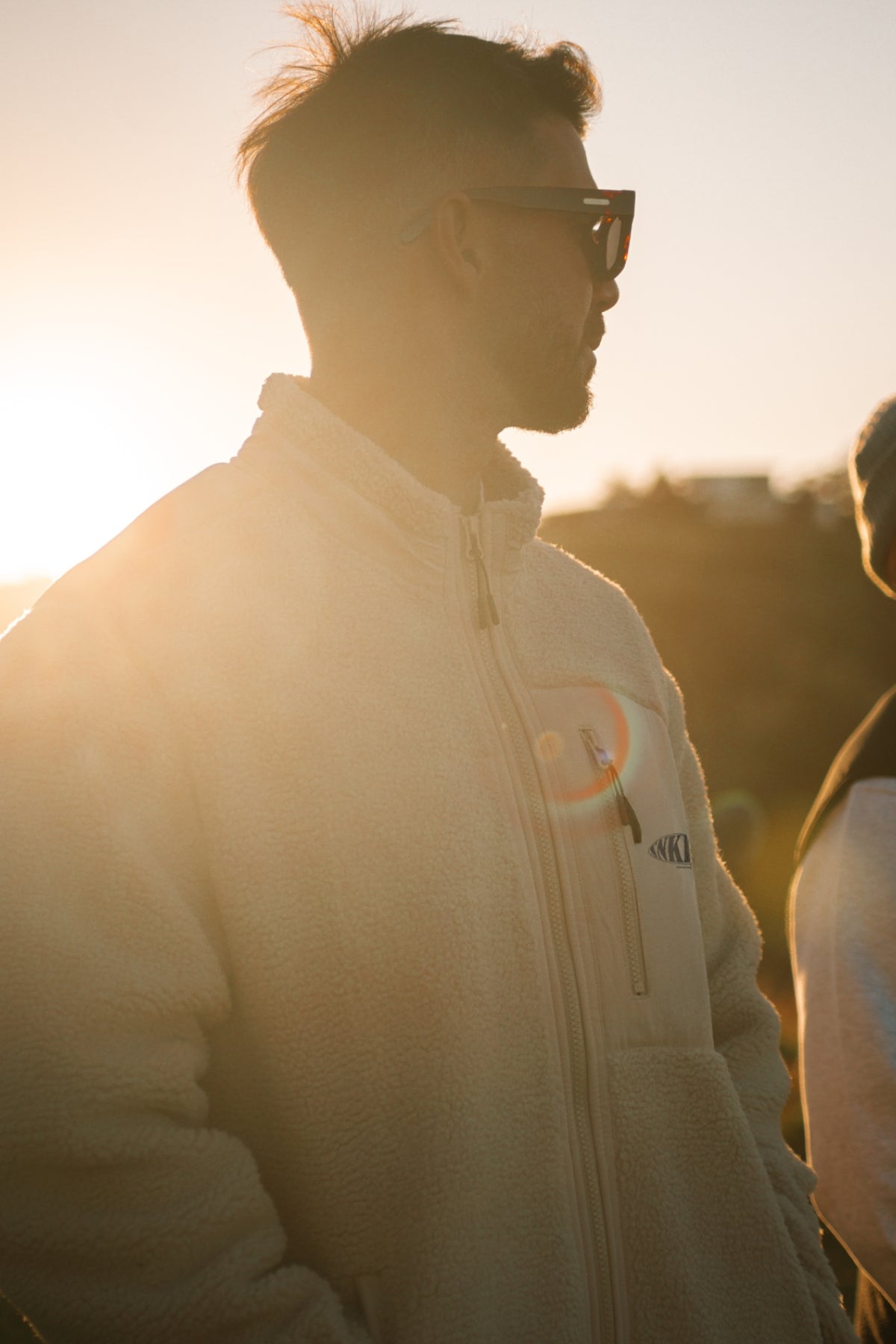 Mann steht vor Sonnenuntergang und trägt fleece jacke in beige 