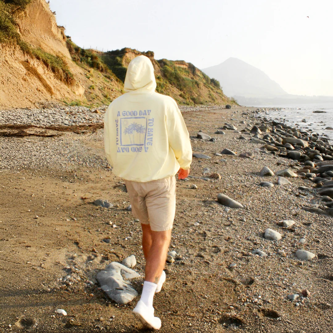 Gelber Hoodie mit Palmenprint – Rückansicht beim Spaziergang am Strand
