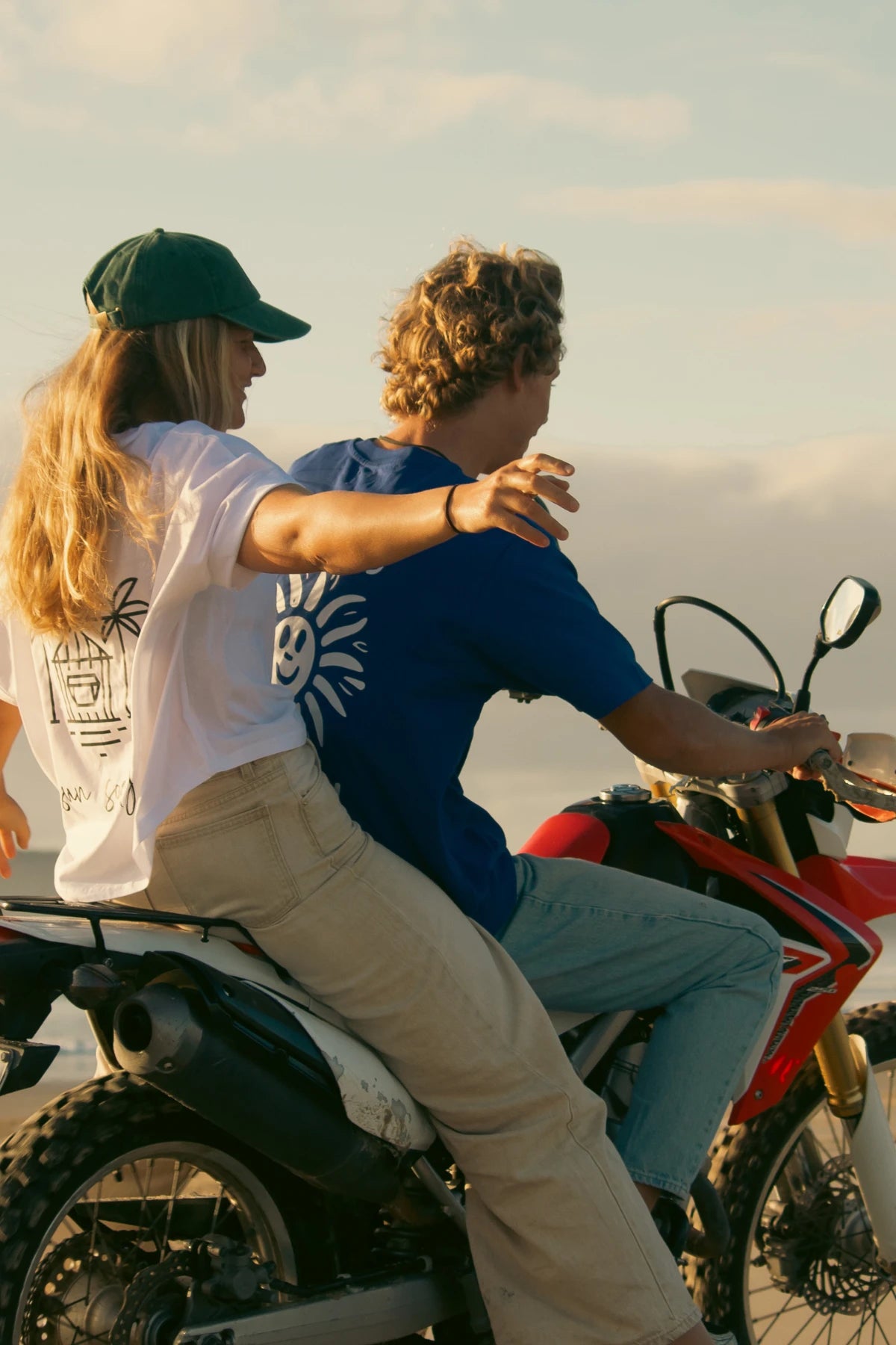 Paar auf Motorrad mit blauem Good Day T-Shirt vor Küstenkulisse