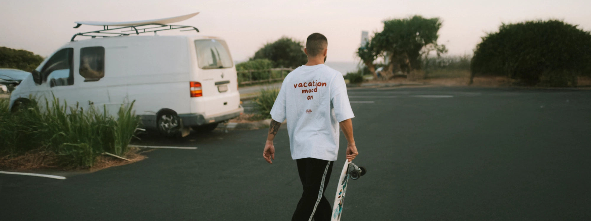 Mann mit Skateboard trägt gaues Oversized T-shirt mit Vacation Mood On Druck